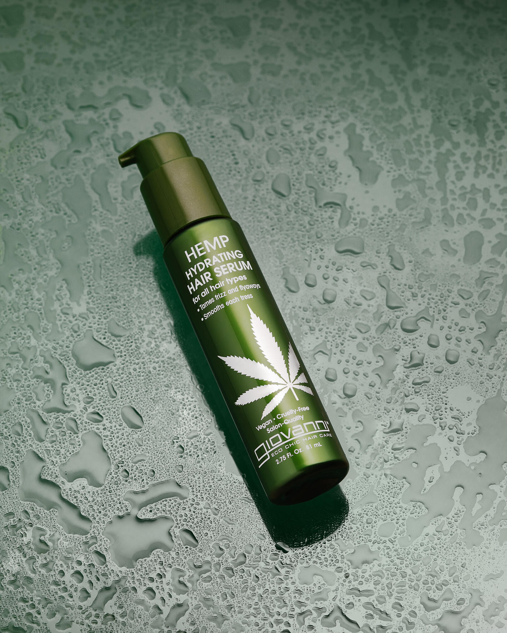 Giovanni Hemo Hydrating hair serum. Giovanni Hemo Hydrating hair serum lies on a green background with water drops. The product has moisturizing properties, which once again highlights the number of drops around the product. There is a shadow under the jar.