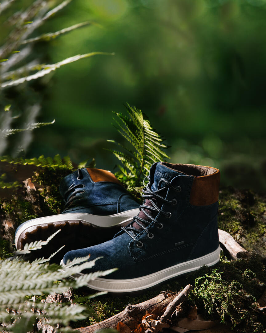 Superfit boots with brown toes and laces stand on sunlit moss. Blue suede Superfit boots with brown toes and laces stand on sunlit moss. The greenery is illuminated by bright sunlight breaking through the foliage of trees.