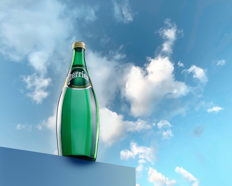 Mineral Water Perrier. A bottle is staying on an edge of something. There are clouds and a blue sky in the background.