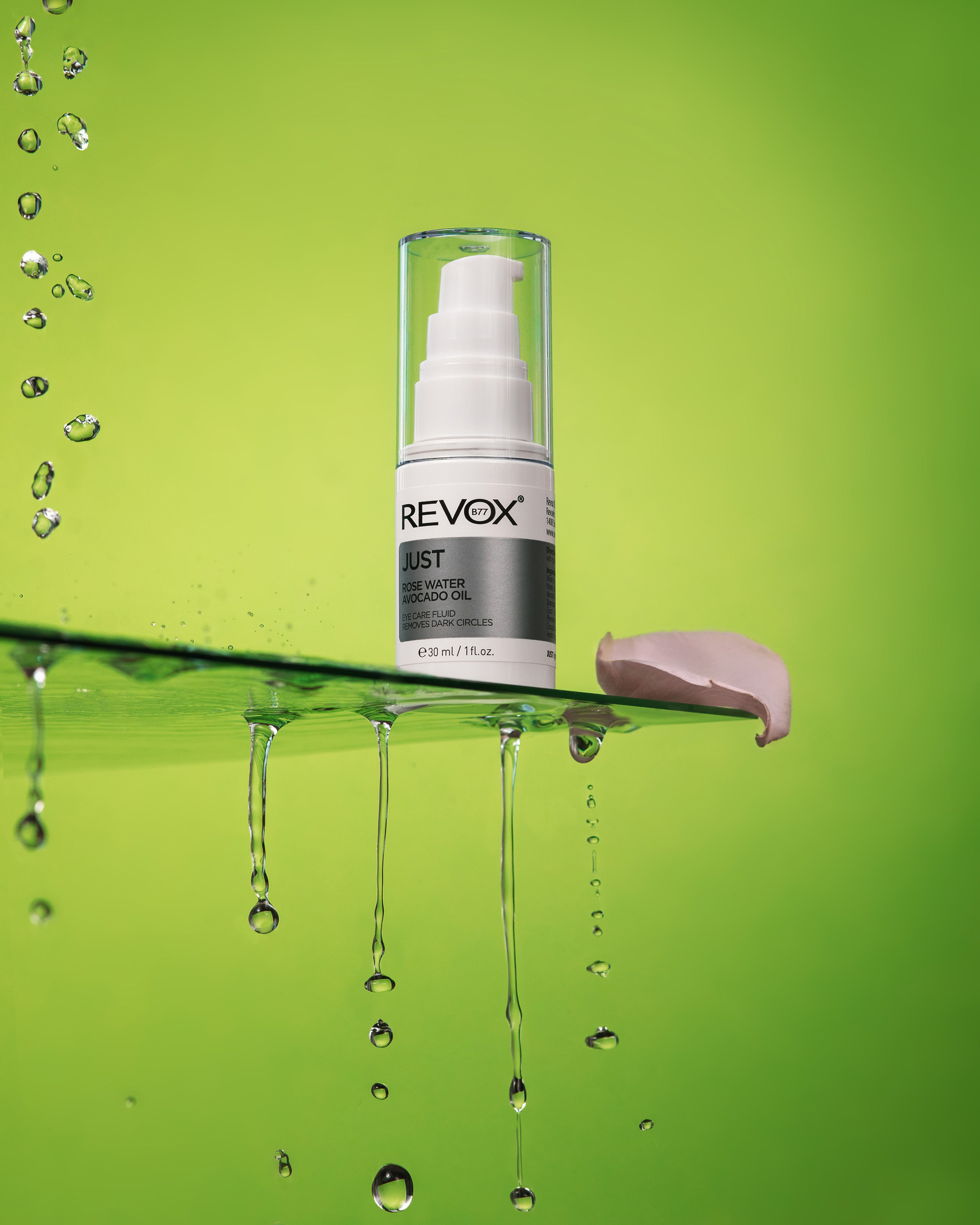 Revox - Just Rose Water Avocado Oil. Бутилка е на ръба на чаша във вода и мехурчета.