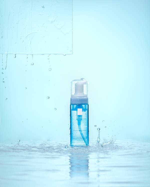 La Roche Posay Mousse. La Roche Posay Mousse. A jar of La Roche Posay Mousse is standing on the water surface, water drops are falling in the backgroun! On the top left is a glass rectangle over which water flows. In the water you can see the reflection from the product
