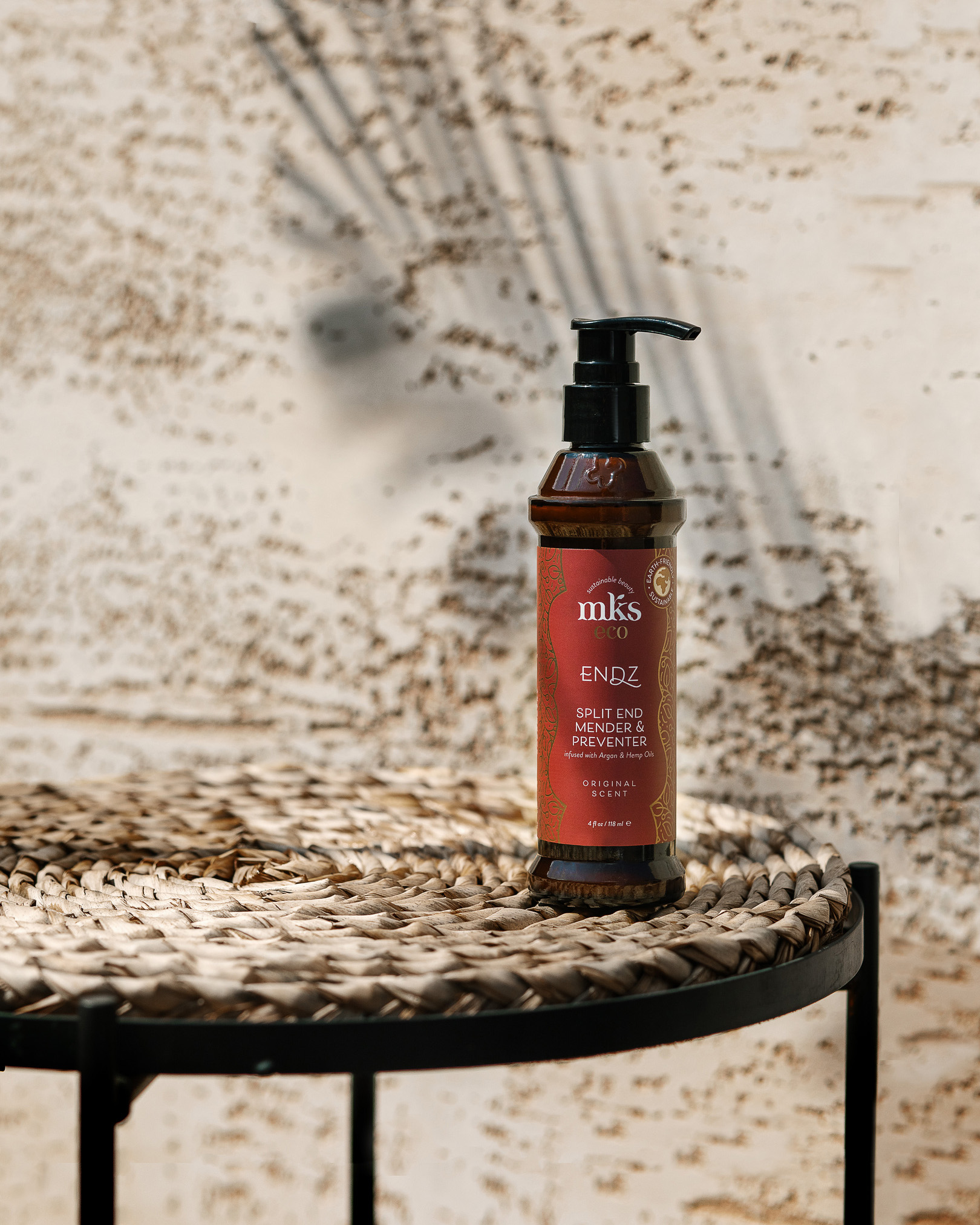 Endz Split End Mender & Preventer. Endz Split End Mender & Preventer! A jar of serum stands in the rays of sunlight on a wicker straw table. In the background is a sandstone wall shaded by palm leaves.