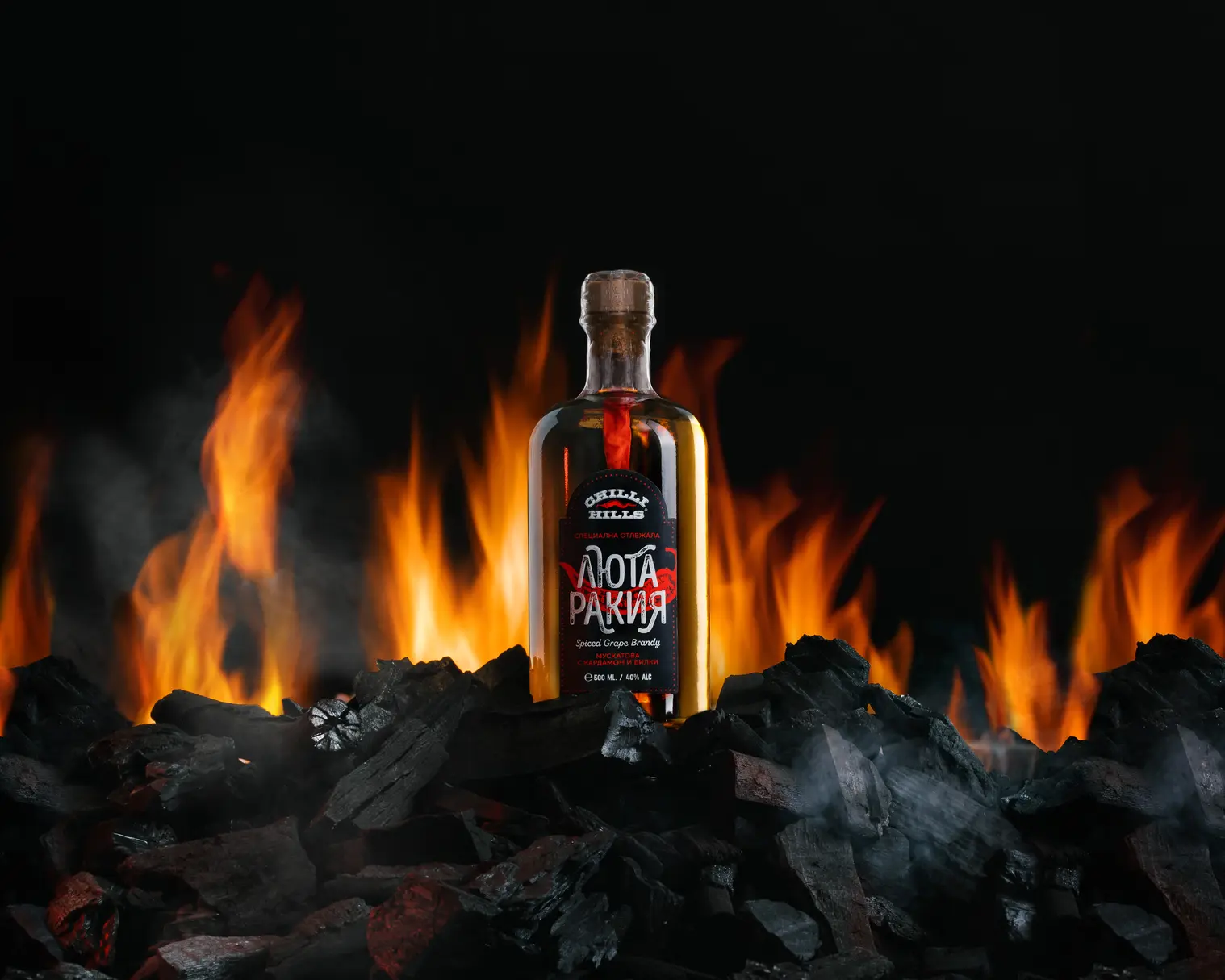 Chilli Hills - Luta Rakia set on fire A bottle of Chilli Hills Rakia sits on smoldering coals. Smoke is visible near the bottle on the right in the foreground. Behind the bottle is a fire, which also shines through a transparent bottle. Pepper is visible inside the bottle.