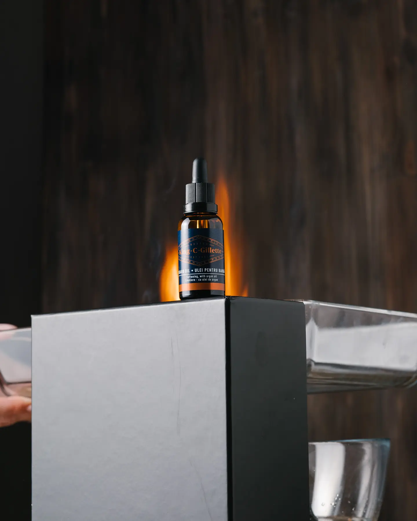 Middle Fire. The photo was taken as a middle flame donor. On the black box is a bottle of King C Gillette of beard oil. It is lit from the left side. A wooden background is visible behind the jar and box.