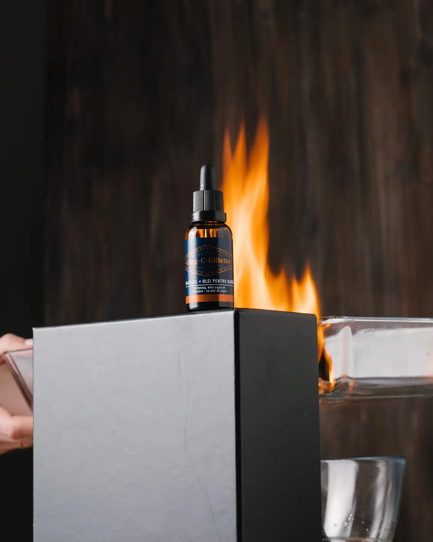 Right Fire. The photo was taken as a right flame donor. On the black box is a bottle of King C Gillette of beard oil. It is lit from the left side. A wooden background is visible behind the jar and box.