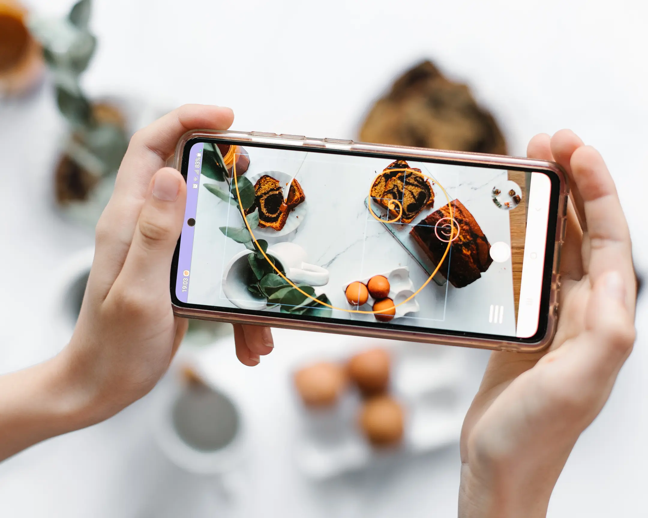 Awesome Photo application - golden spiral. A person holding a phone demonstrating the Awesome Photo application and a golden spiral, cakes, eggs, and leaves.