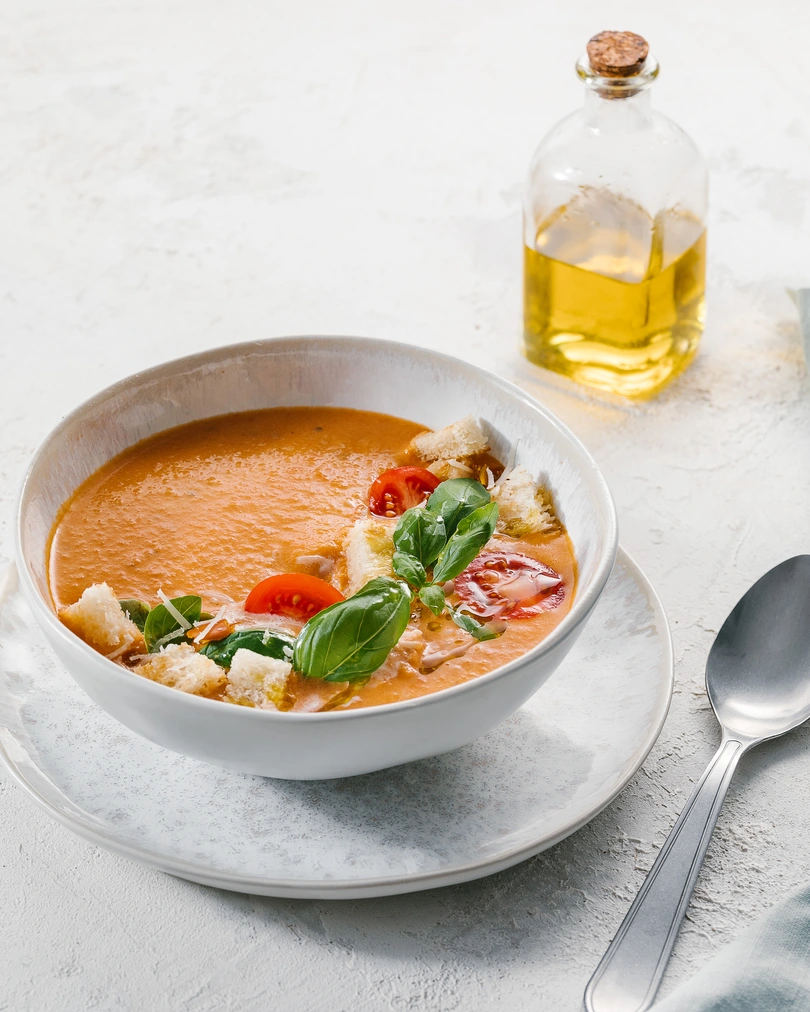 Печена супа. В чинията е показана доматена супа отблизо. Гарнира се с крутони от бял хляб, зехтин и чери домати. На заден план на снимката има съд за зехтин.