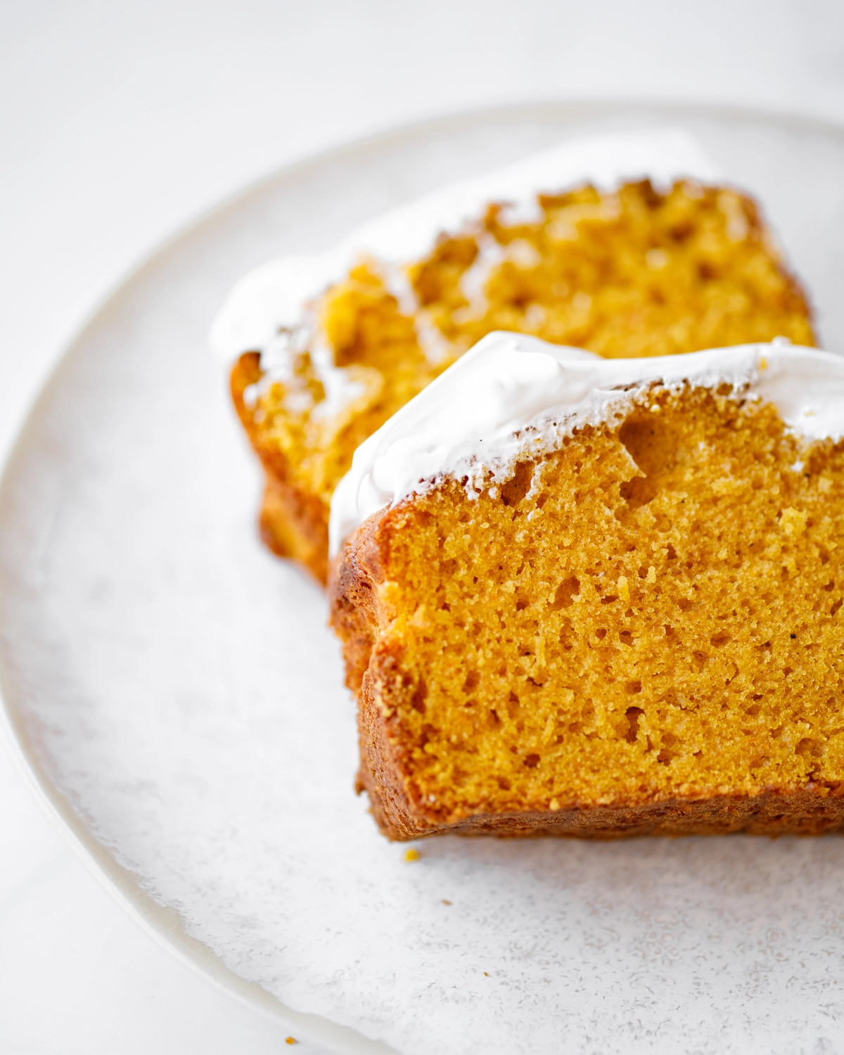 Pumpkin bread. There are 2 slices of pumpkin bread on the plate. Its delicate texture and delightful orange color are visible.