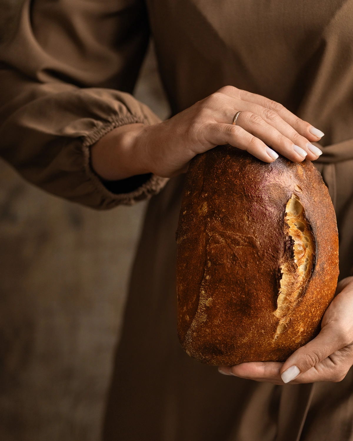 Домашен хляб. Жена в кафява рокля държи домашен хляб в ръцете си.