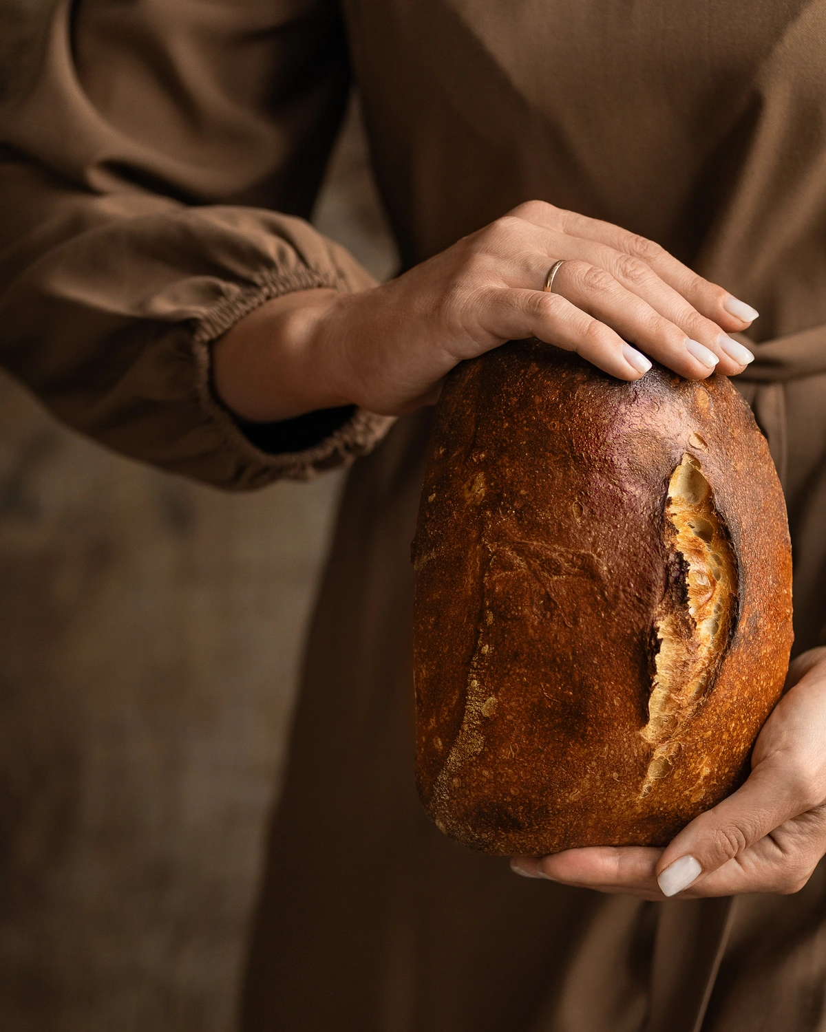 Рomemade bread. A woman in a brown dress holds homemade bread in her hands.