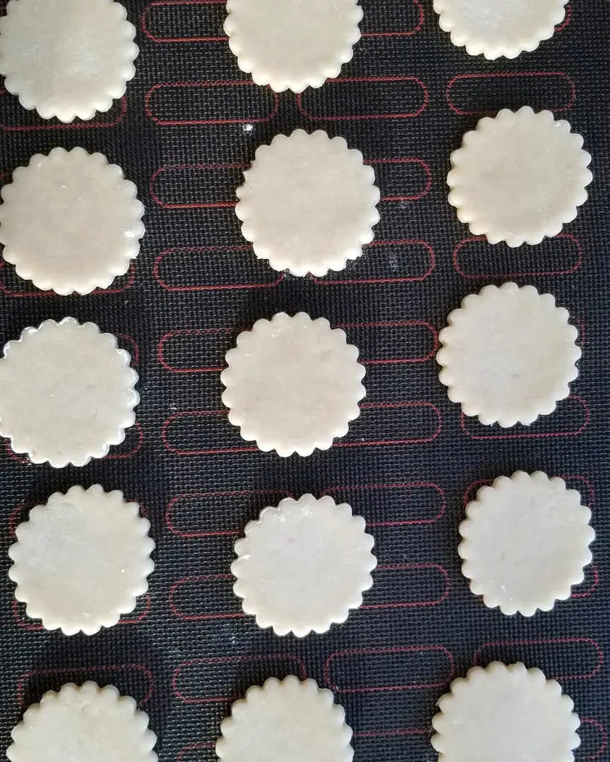 Бисквитките, изрязани от тестото, се поставят върху перфорирана подложка. Бисквитките, изрязани от тестото, се поставят върху перфорирана подложка.