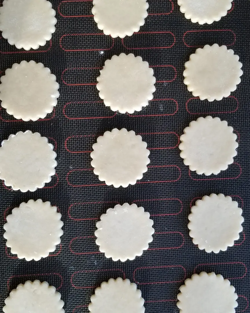 Cookies cut out of dough lie on a perforated mat. Cookies cut out of dough lie on a perforated mat.