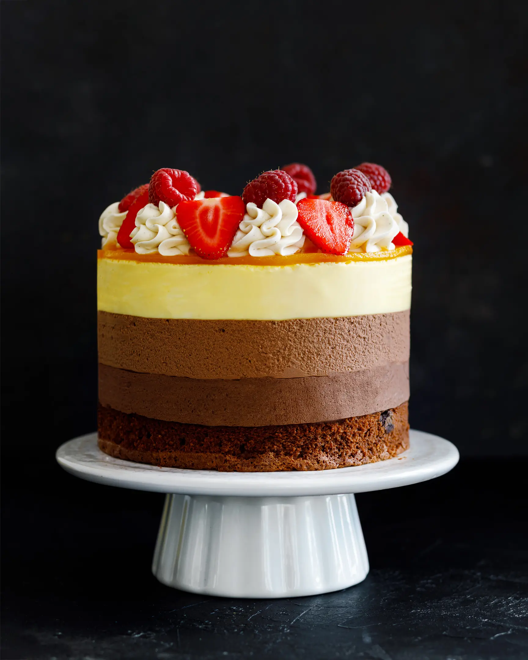 The photo shows a three-chocolate cake.  Full view. The photo shows a three-chocolate cake. All three layers of different colors are visible. The cake is decorated with raspberries and strawberries.