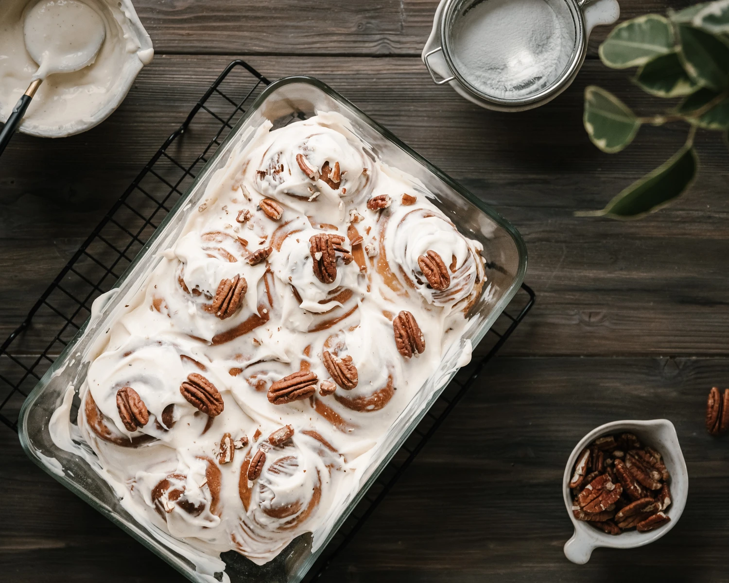 Buns covered with icing are on a wooden table. There is a glass form with buns on the table. The buns are covered with icing.