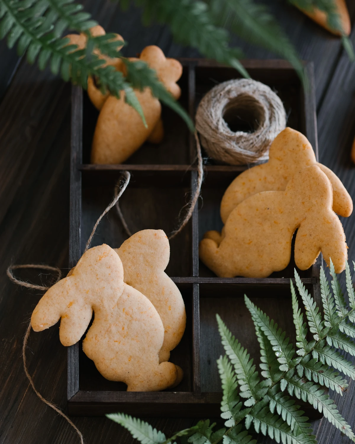 Pumpkin cookies in the shape of a hare. View from above. Hare-shaped cookies lie on a wooden surface in a wooden tray. There is moss and fern around - they imitate being in the forest. View from above.