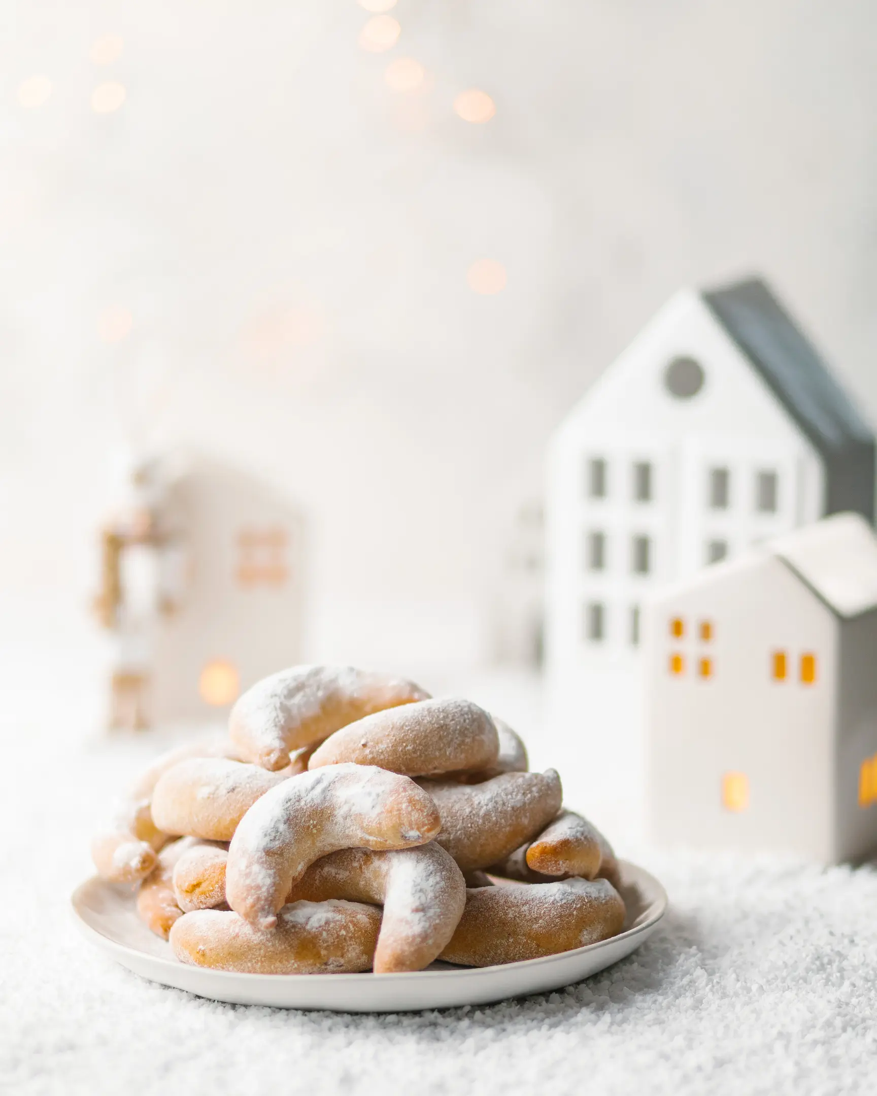 On the table is a plate of crescent-shaped cookies. On the table is a plate of crescent-shaped cookies. Next to the cockies are ceramic houses.