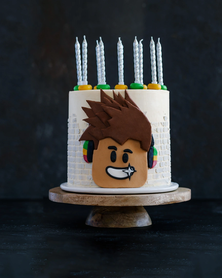 Cake cream for covering. On a dark background - is a ceramic stand stands a cake decorated with candles. On the surface of the cake, a picture of a smiling young man is used as decor.