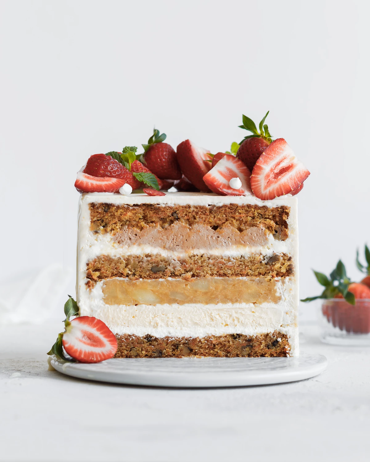 Carrot cake with apple layer. There is a cake on the table. It is decorated with strawberries. Visible carrot cakes, apple layers, and chocolate cream pyramids between layers of carrot cakes.