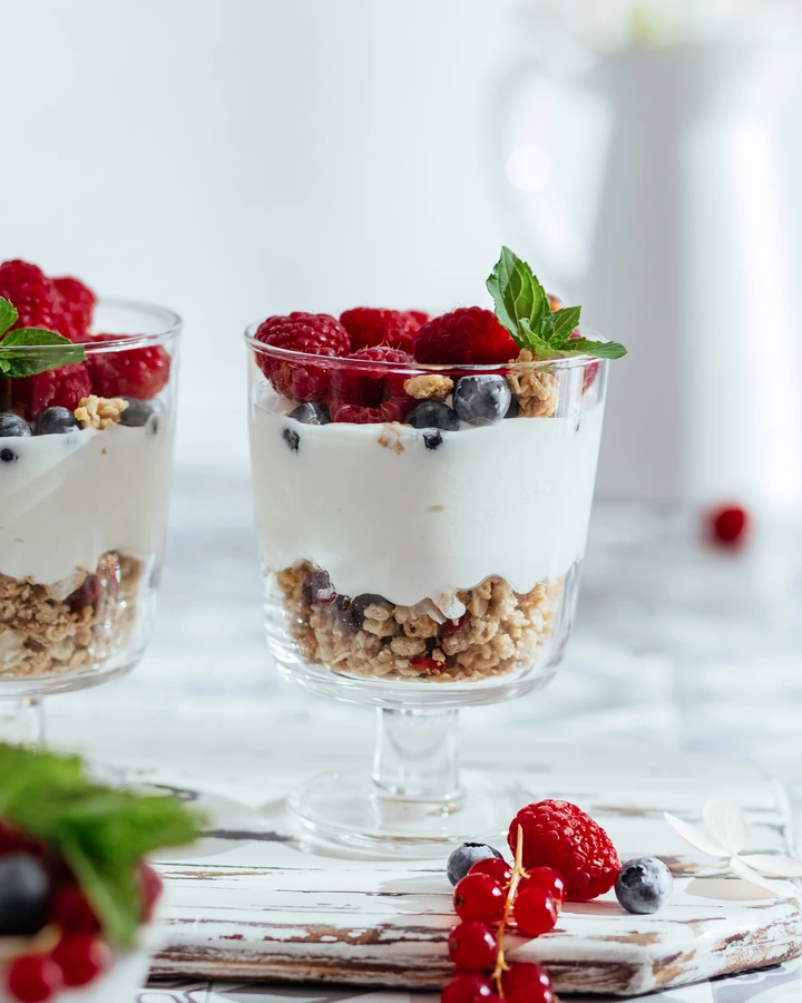 Crunchy breakfast granola. 2 cups filled with granola. On top of the granola is a layer of yogurt. There are many berries on top. 