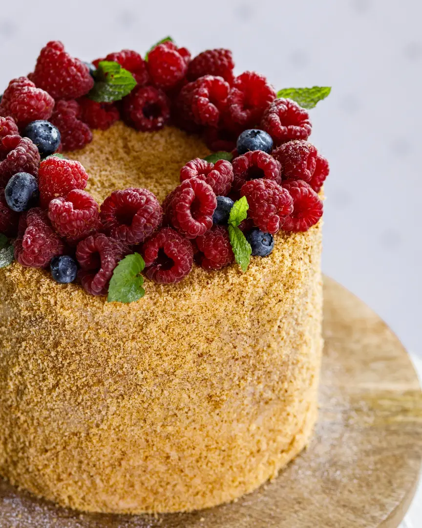 Part of honey cake. On a  wooden cake stand standing Russian honey cake. On the cake stand is a cake sprinkled with honey crumbs. The cake is topped with a ring of berries and mint.