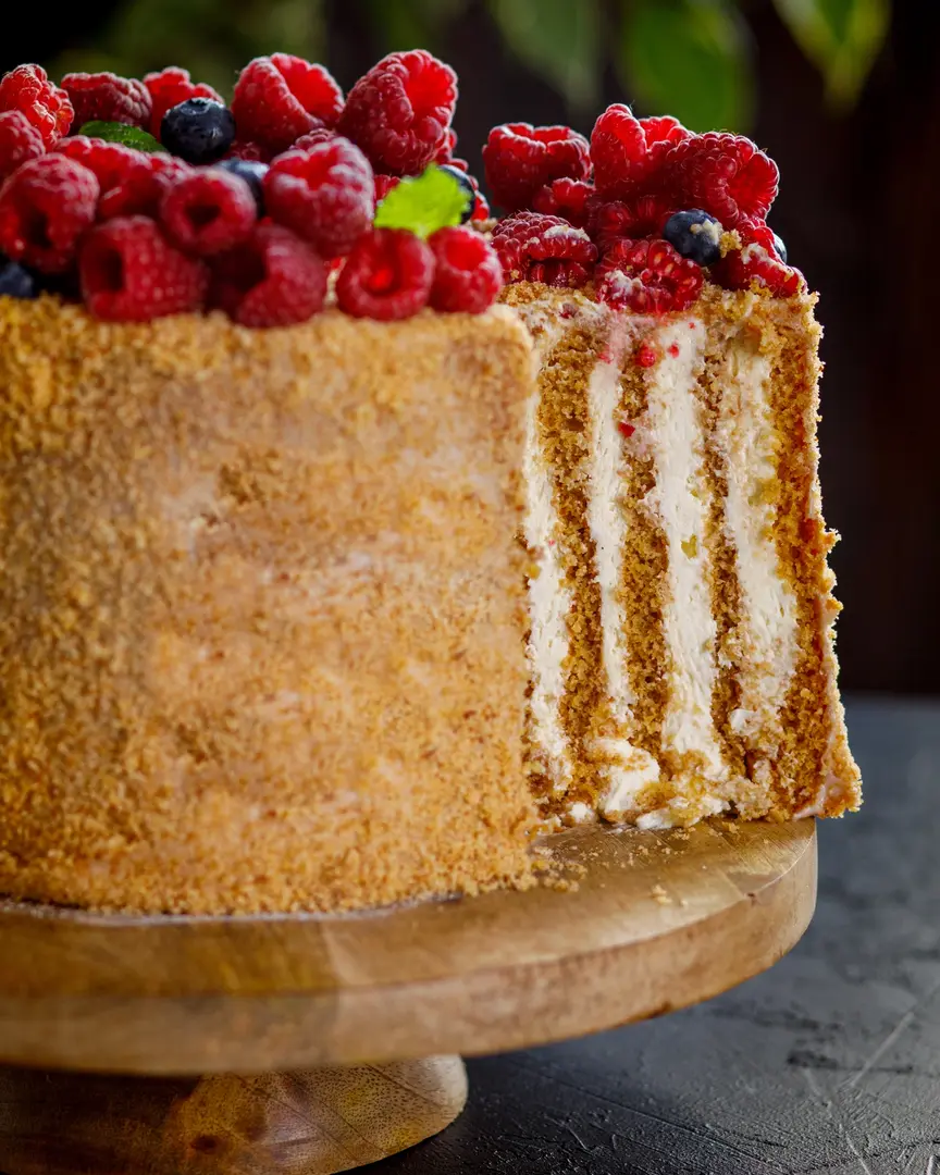 На тъмен фон стойте парче медена торта. На маса с тъмна текстура има кафява дървена поставка за торта. На поставката за торта има торта, поръсена с медени трохи. Отгоре тортата се украсява с ринг от горски плодове и мента.
Тортата се разрязва. Вниманието на зрителя е осигурено с нестандартно - вертикално подреждане на кори в тортата