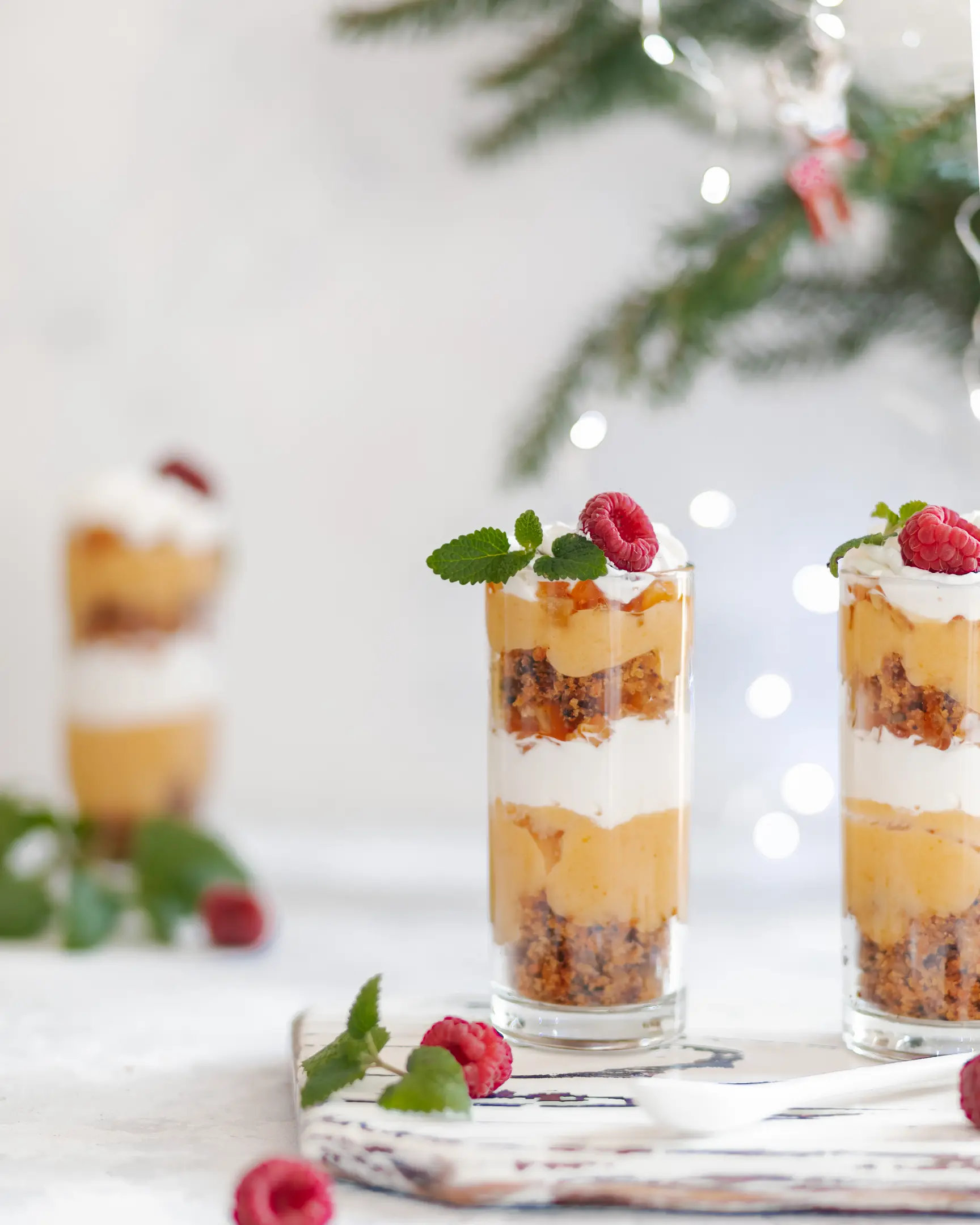 There are trifles on a wooden cutting board.  There are trifles on a wooden cutting board. Behind them are glowing Christmas lights.