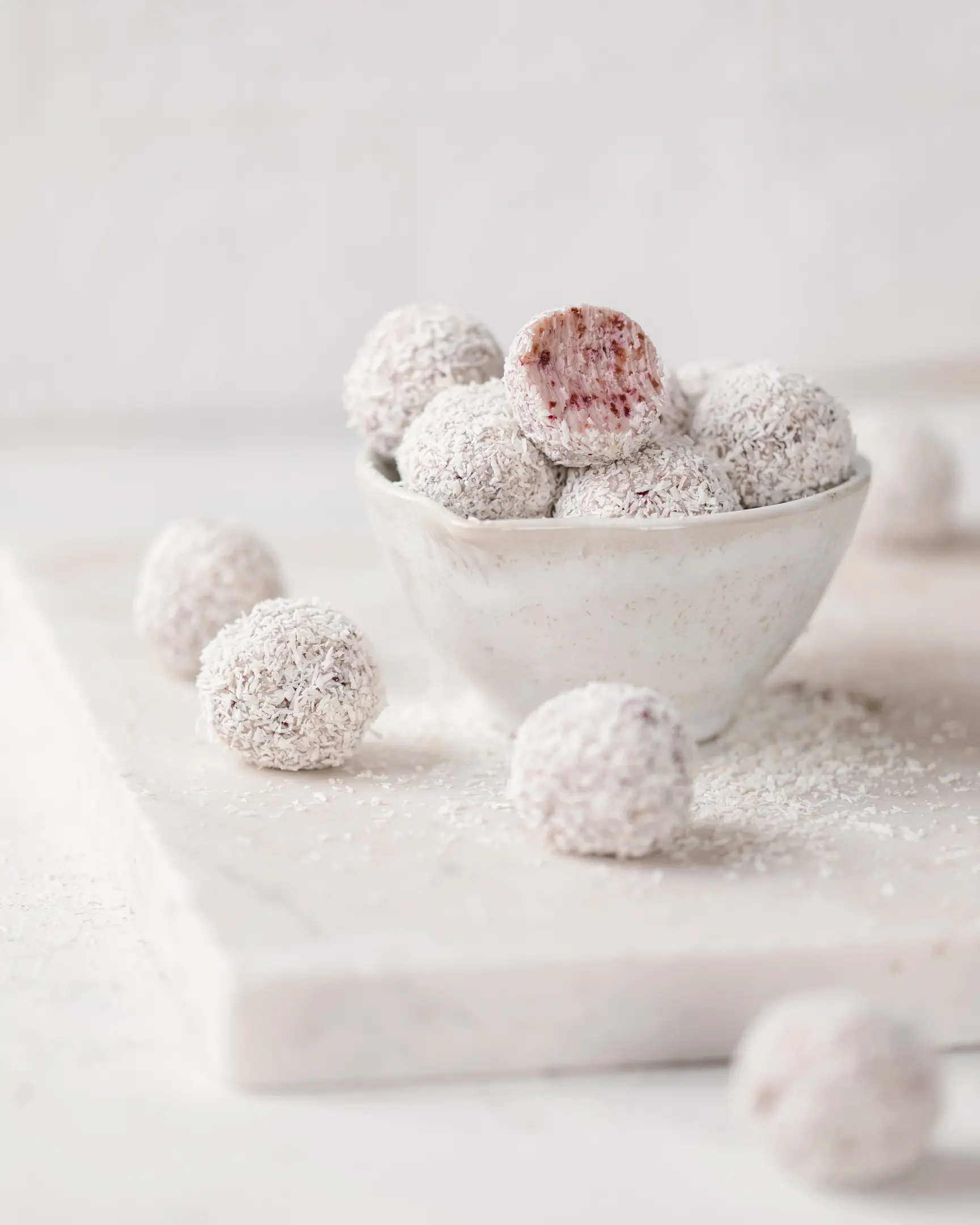 Truffles lie in a deep plate on a light background. Truffles lie in a deep plate on a light background. Several truffles lie on the table. One of the truffles is cut open and you can see the texture with pieces of cranberries. Each truffle is covered in coconut flakes.