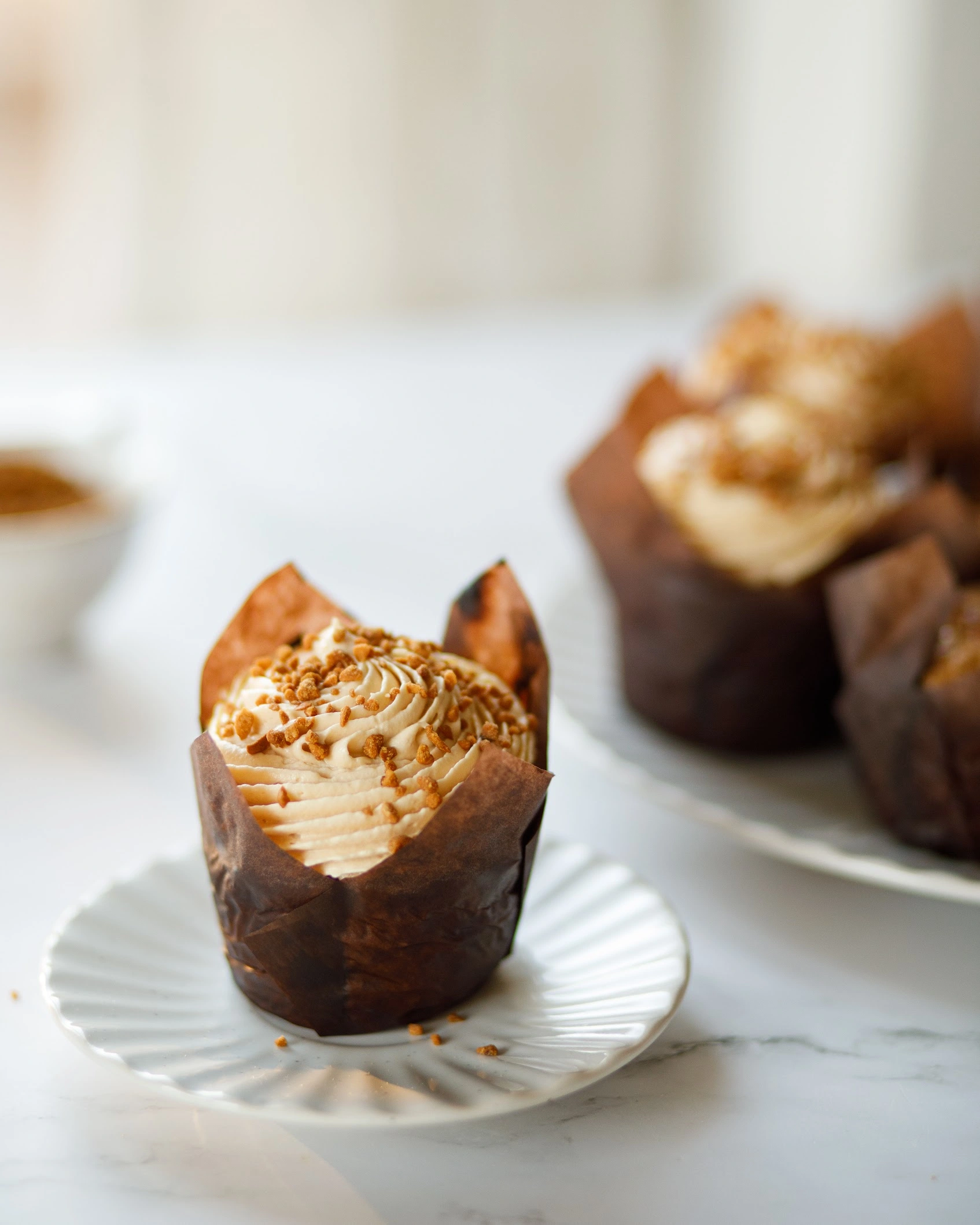 Pumpking muffin on the table. On the marble table, there is a small plate on which there is a pumpkin cupcake. The cupcake is decorated with a creamy cap based on boiled condensed milk.