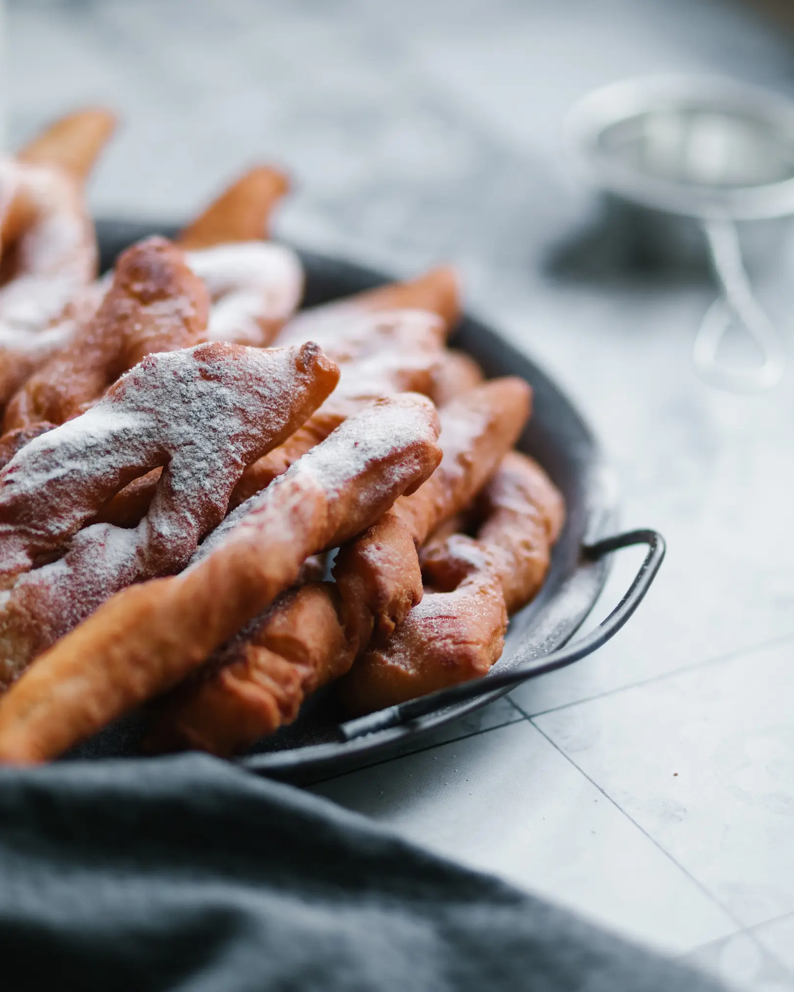 On the table is a metal plate with handles. On the table is a metal plate with handles. On it lies a ruddy hvorost. The hvorost is sprinkled with powdered sugar and cinnamon.