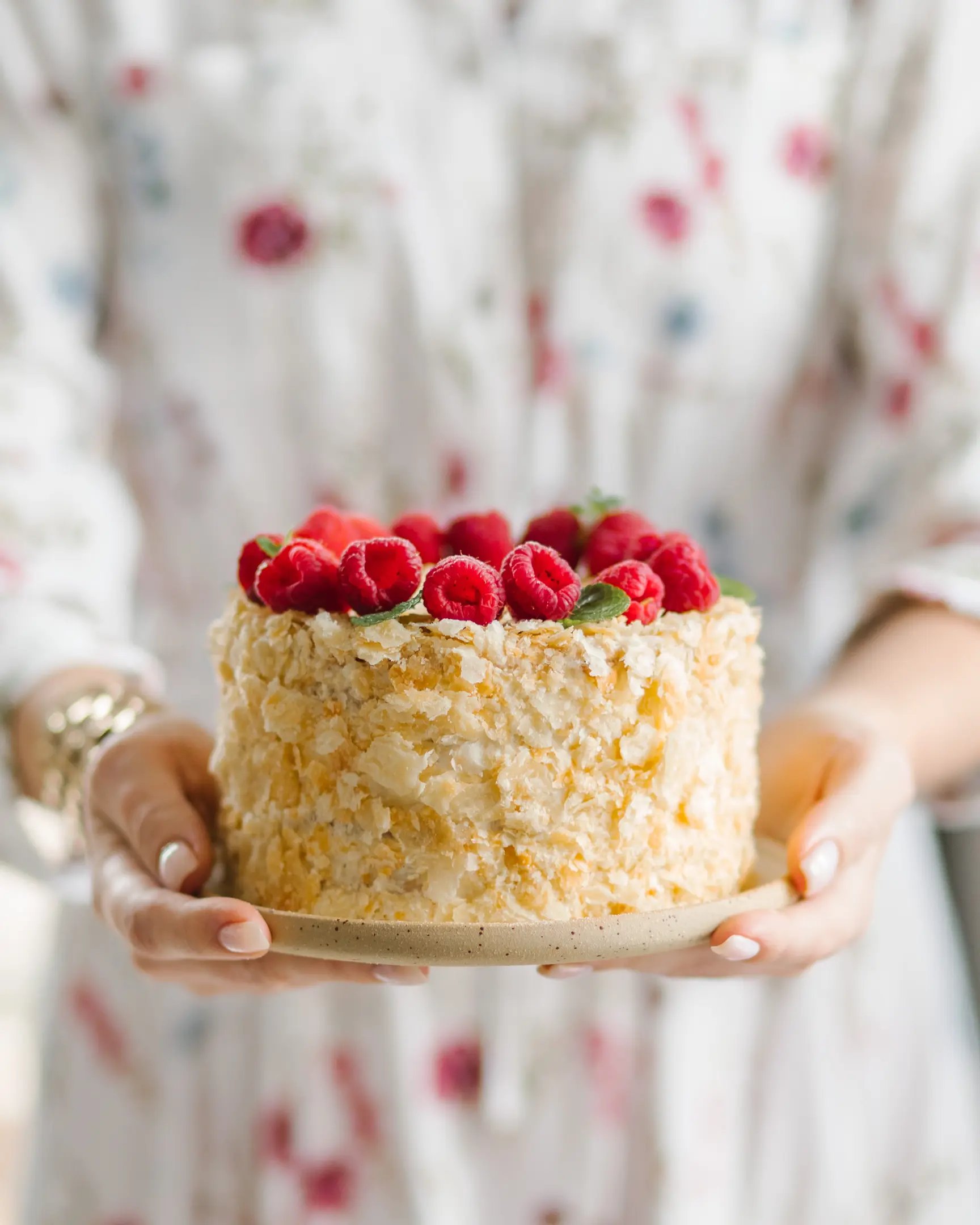 A woman holds Napoleon cake in her hands. A woman holds a cake in her hands. The cake is decorated with fresh raspberries.