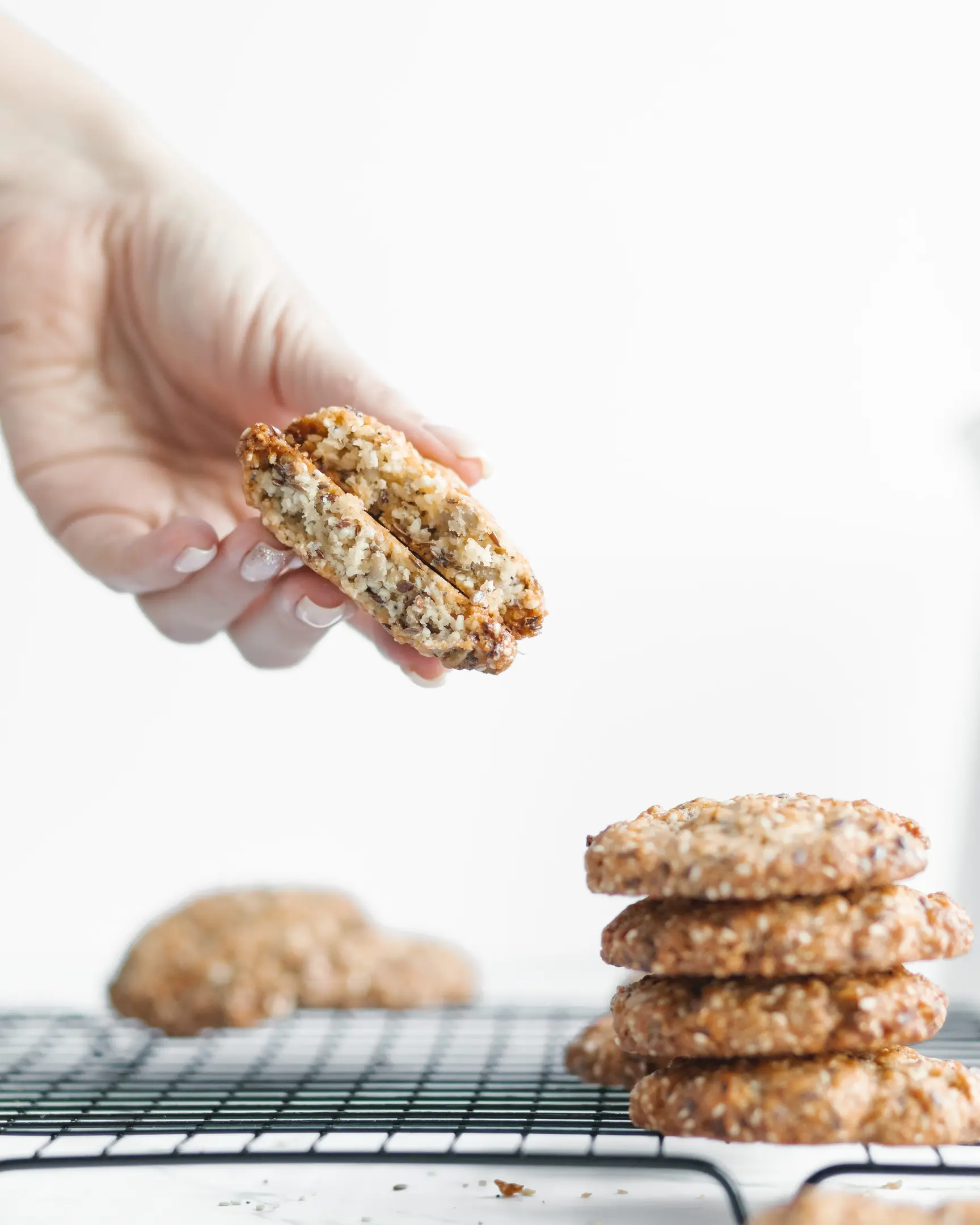 A woman holds a cookie in her hand. A woman holds a cookie in her hand. Below the hand are the same cookies. They are on the baking rack.