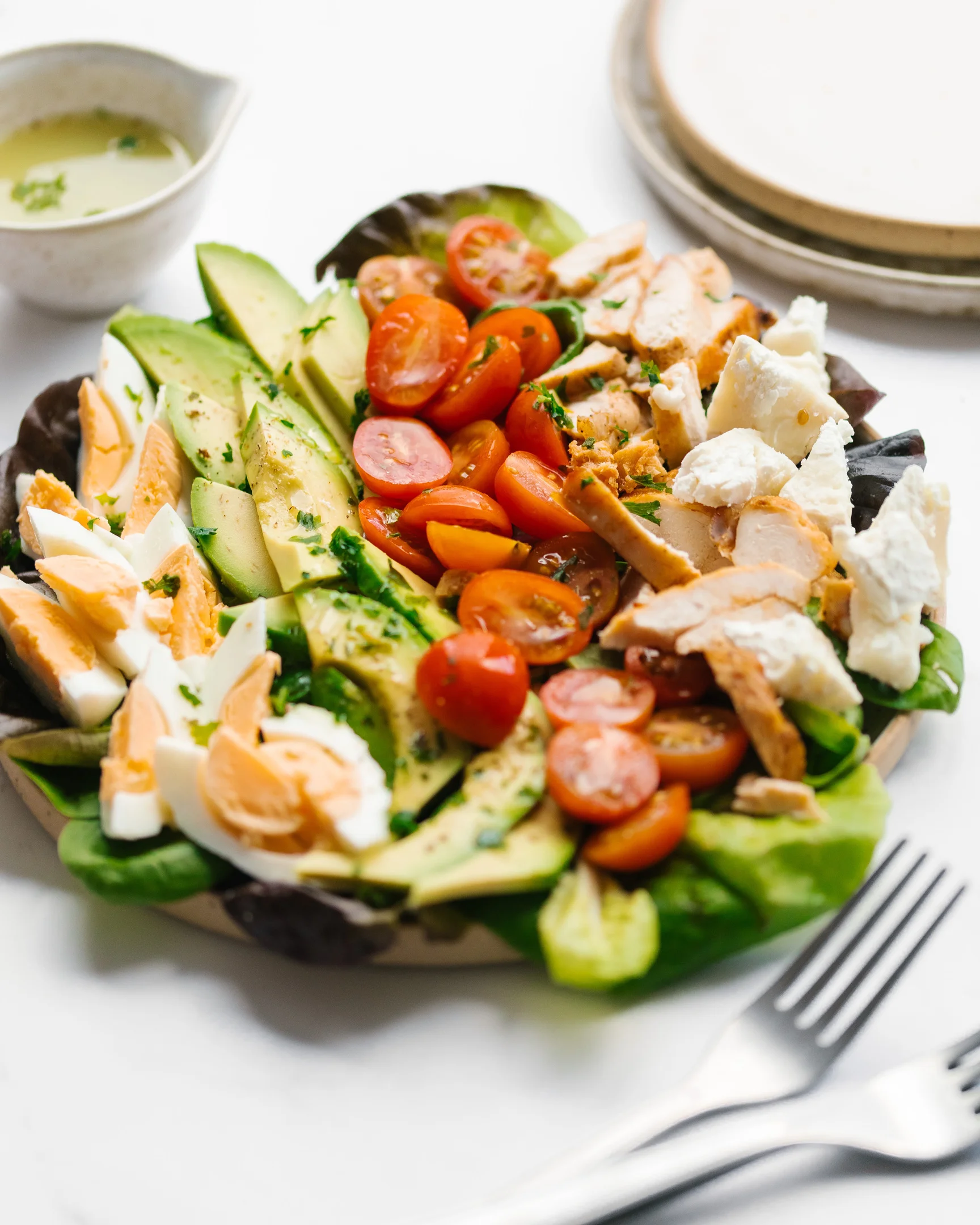 Cobb salad On the table is a plate with ingredients laid out in a line. Behind the plate is the salad dressing.