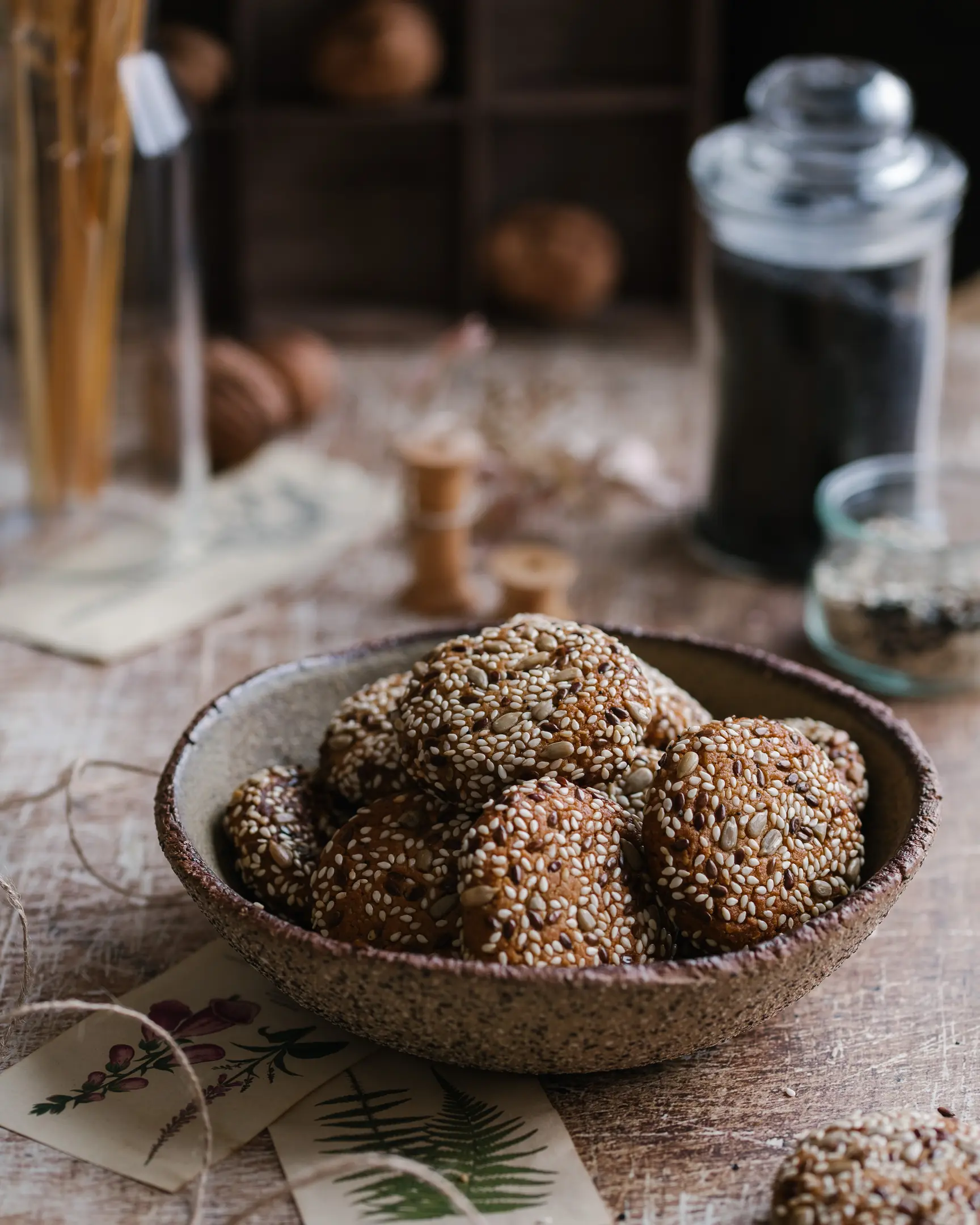 Vegan tahini cookies On the table is a plate full of cookies. Cookies decorated with seeds. In the background is a jar of black sesame seeds and wooden elements.