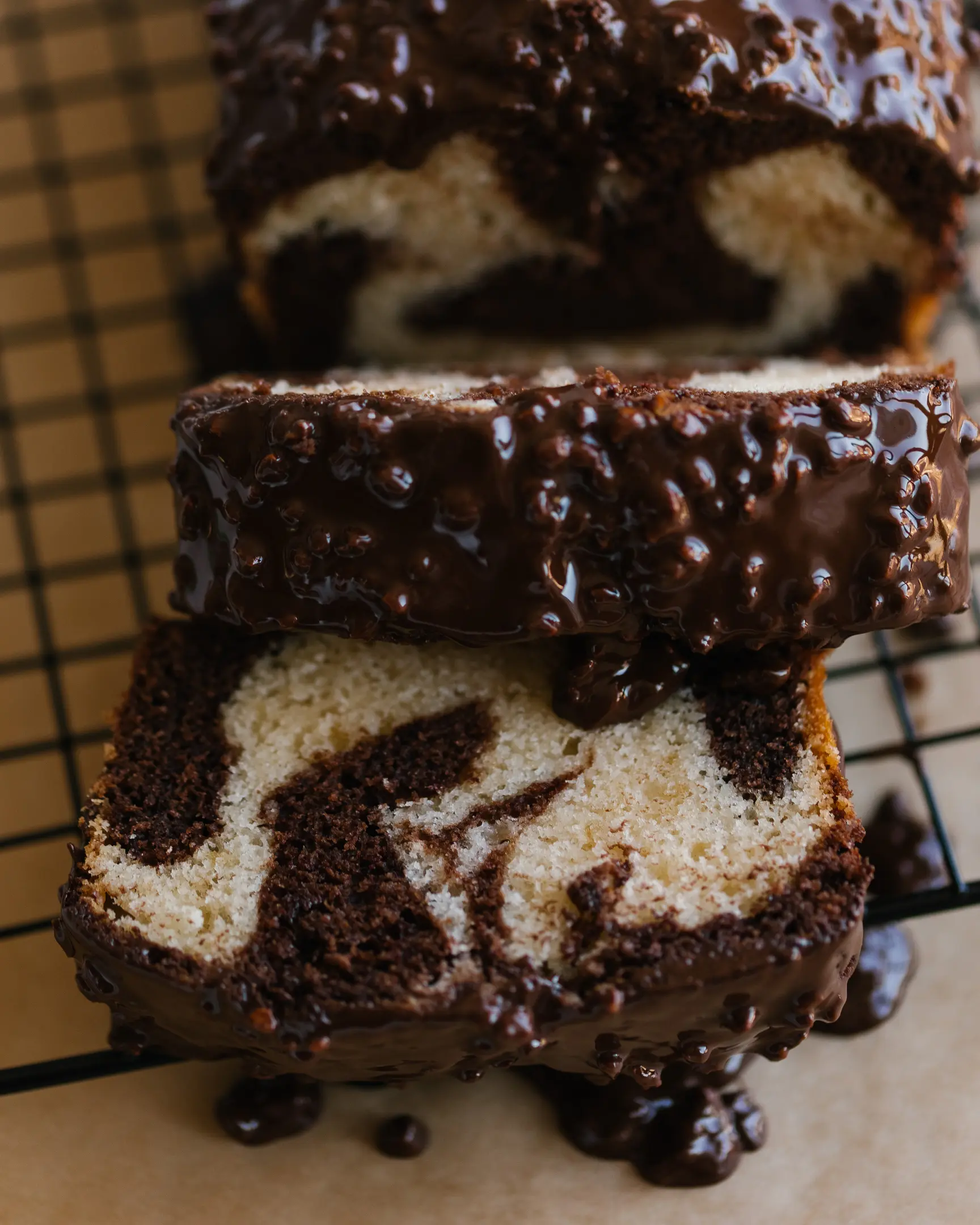 A sliced marble cake lies on a pastry rack to cool. A sliced marble cake lies on a pastry rack to cool. The cake is cut into slices. There is a knife next to the cupcake. It's covered in chocolate icing. Drops of chocolate under the cupcake.