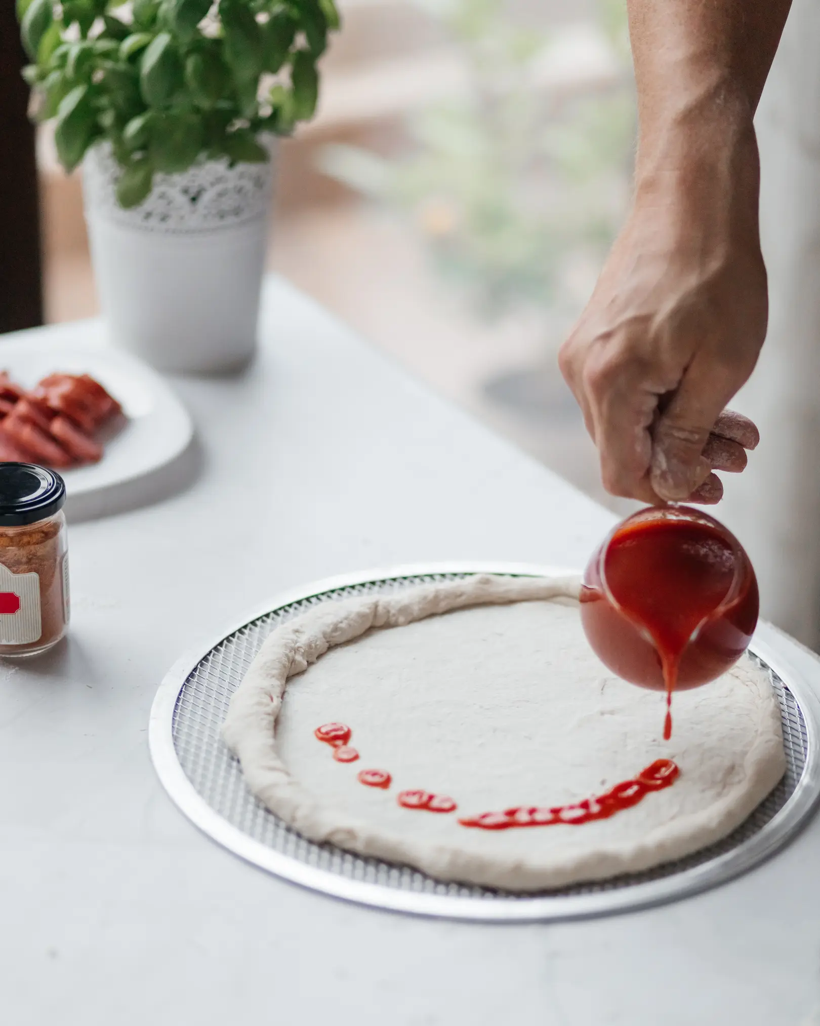 A man pours tomato sauce over  pizza dough. A man pours tomato sauce over pizza dough.