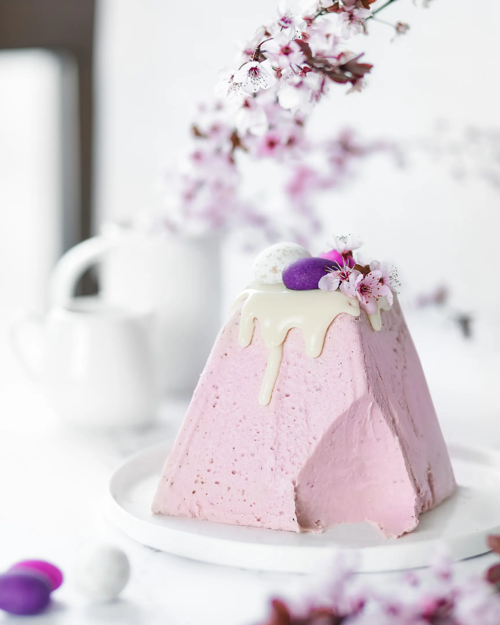 Russian raspberry-curd Easter. Russian raspberry-curd Easter is on the table. Cherry blossoms are visible in the background. Cottage cheese Easter decorated with pink and blue chocolate eggs.