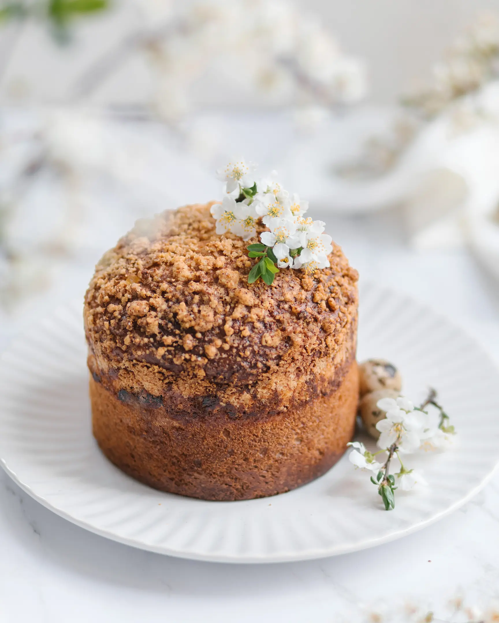 There is Christmas bread on the table. There is Easter bread on the table. It is decorated with cherry blossoms and powdered sugar. Next to the kozunak are quail eggs and a cherry branch.