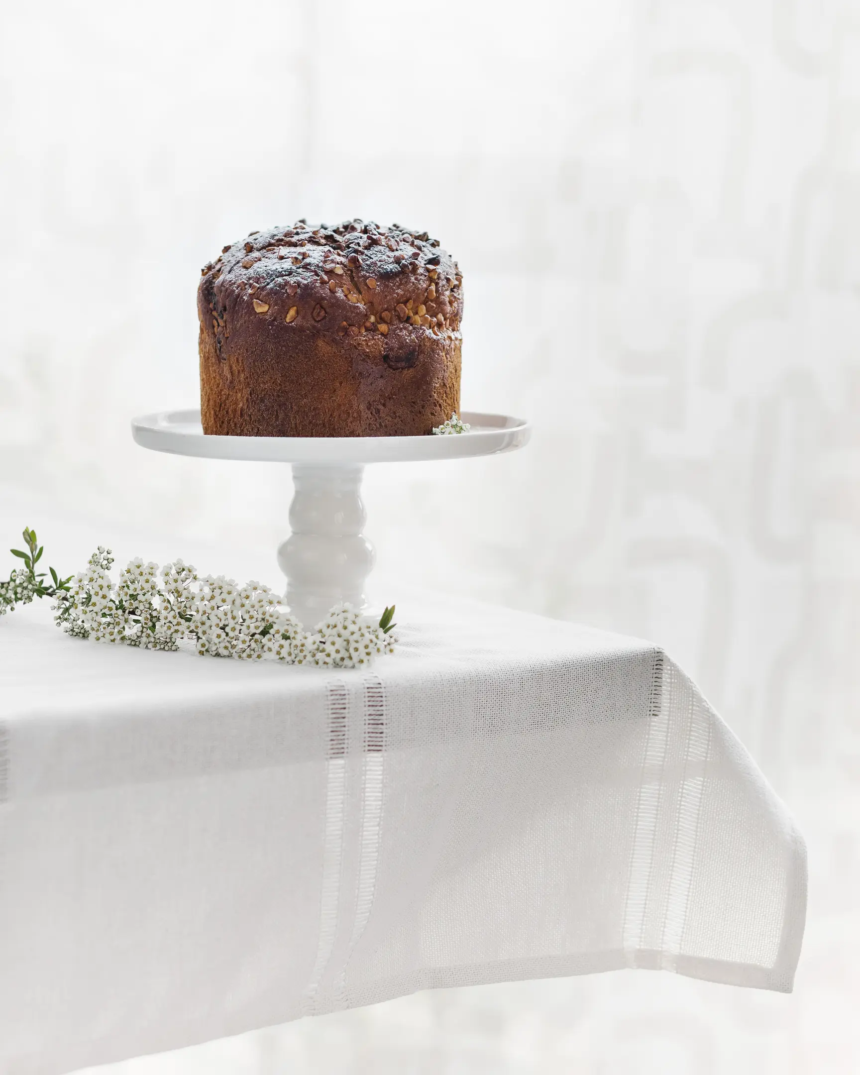 The Easter bread is on the table.  The Easter bread is on the table. The table is covered with a light festive tablecloth. There are spring flowers on the table.