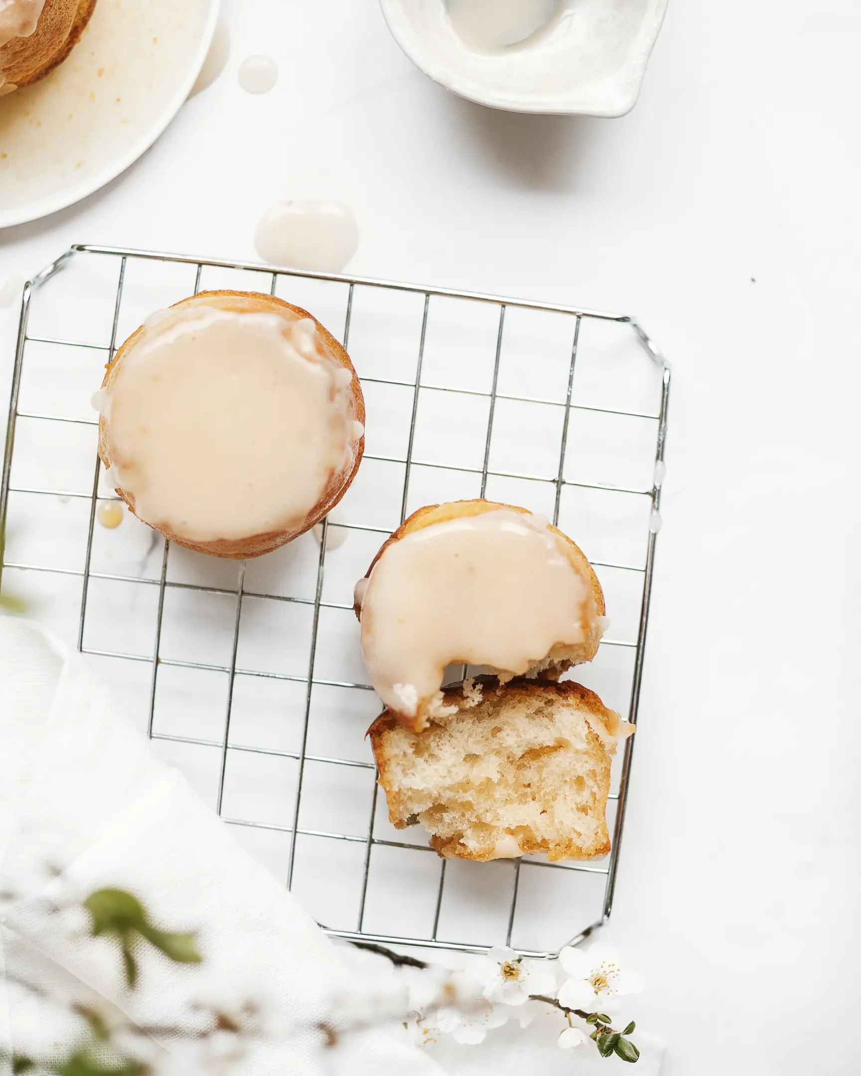 On the confectionery grate for cooling are rum baba. On the confectionery grate for cooling are rum baba. Flowers are visible in the foreground. View from above. One rum baba is broken. You can see the texture of the dough. Buns are covered with light glaze.