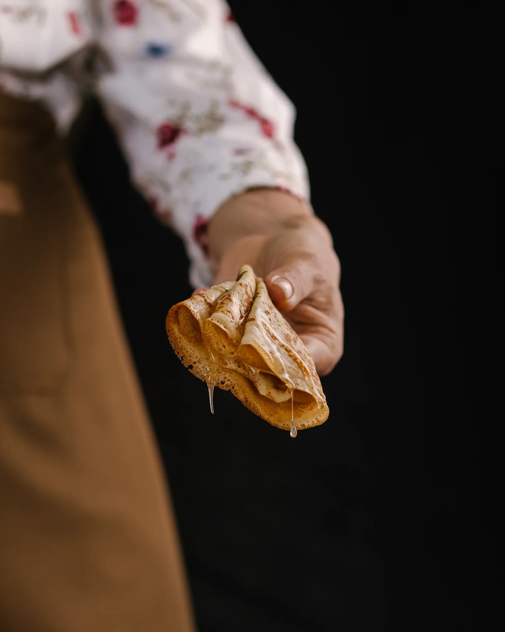 A woman holds a fork in her hand, on which a pancake has been pricked. A woman holds a fork in her hand, on which a pancake has been pricked. The pancake is poured with honey. Honey drips from the pancake. Honey glitters in the rays of light.