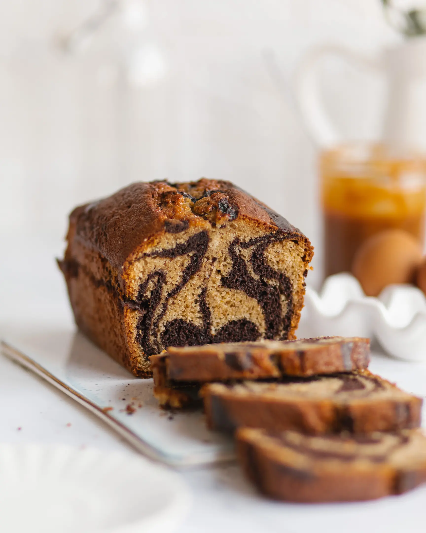 A marble cupcake is on the table. A marble cupcake is on the table. In the background, you can see caramel in a jar. The cupcake is cut. You can see the marble pattern and texture of the cupcake.