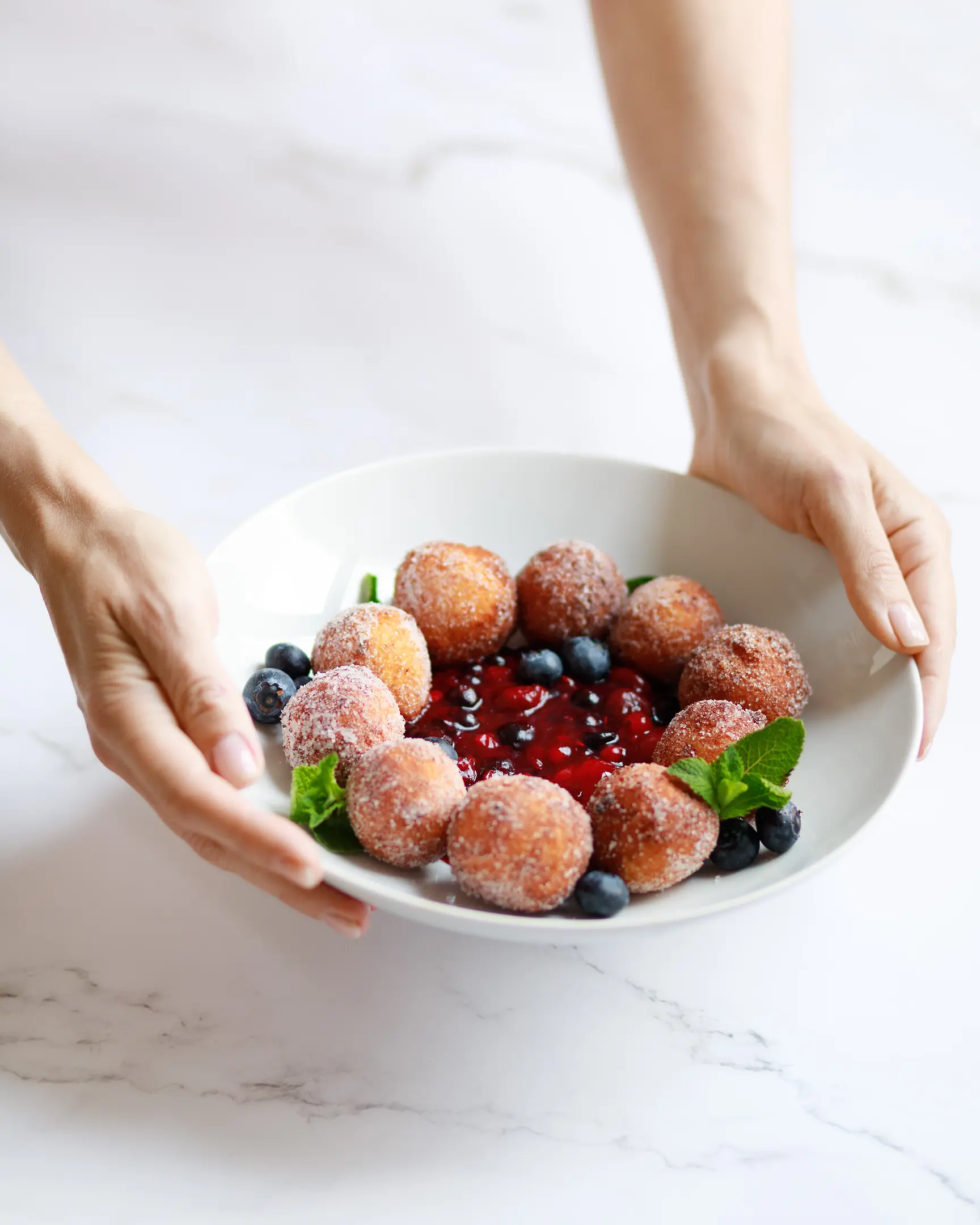 A woman holding plate with donuts and berries jam in her hands. A woman holding a plate with donuts and berries jam in her hands.