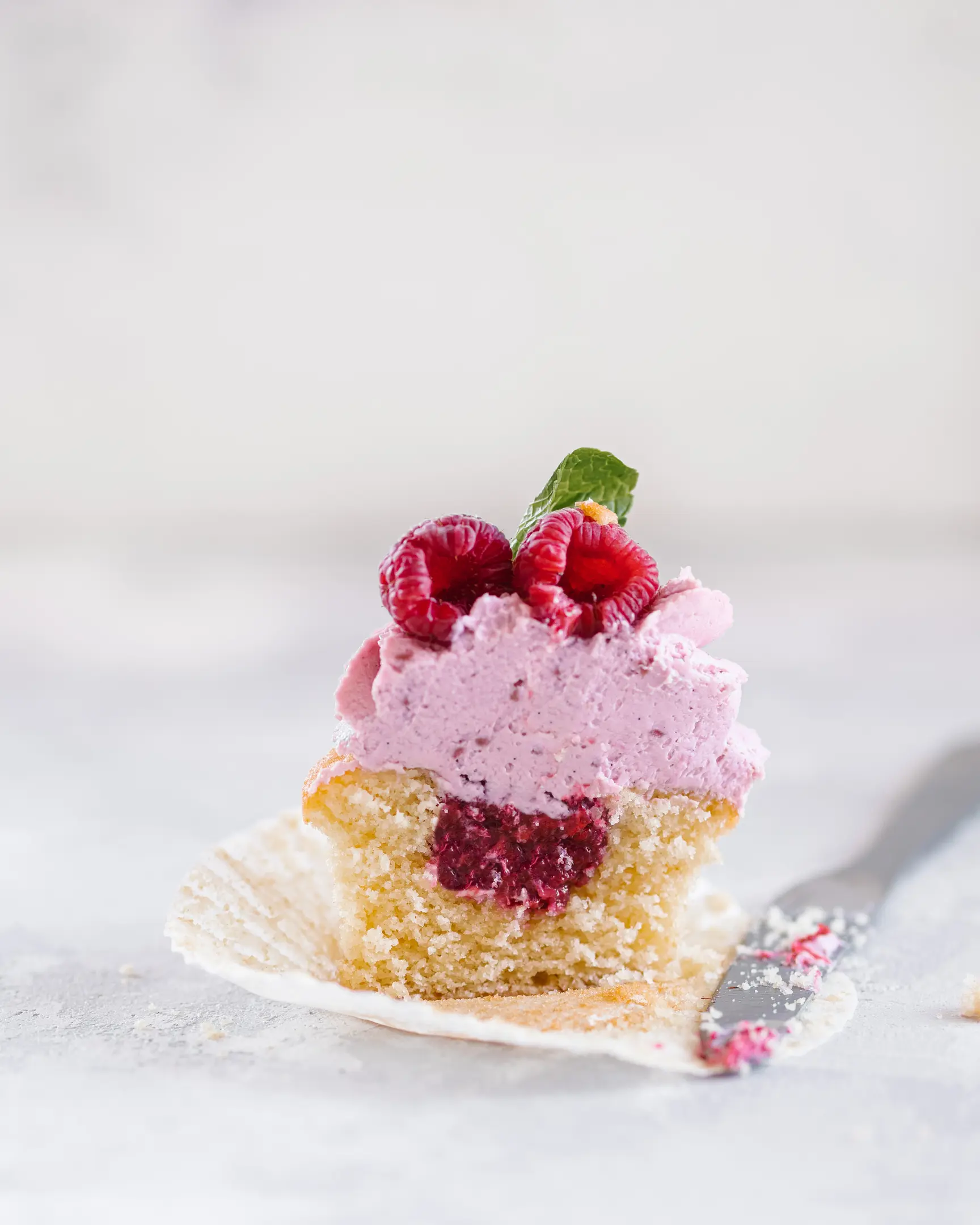 There is a muffin on the plate.  There is a muffin on the plate. It's cut. You can see the raspberry filling inside. There is a knife nearby.