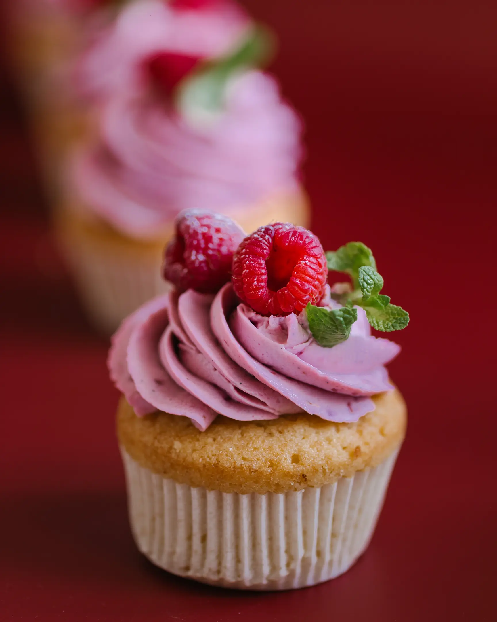 Cupcakes stand on a dark red background one behind the other. 3 cupcakes stand on a dark red background one behind the other. They are decorated with raspberry cream and raspberries.