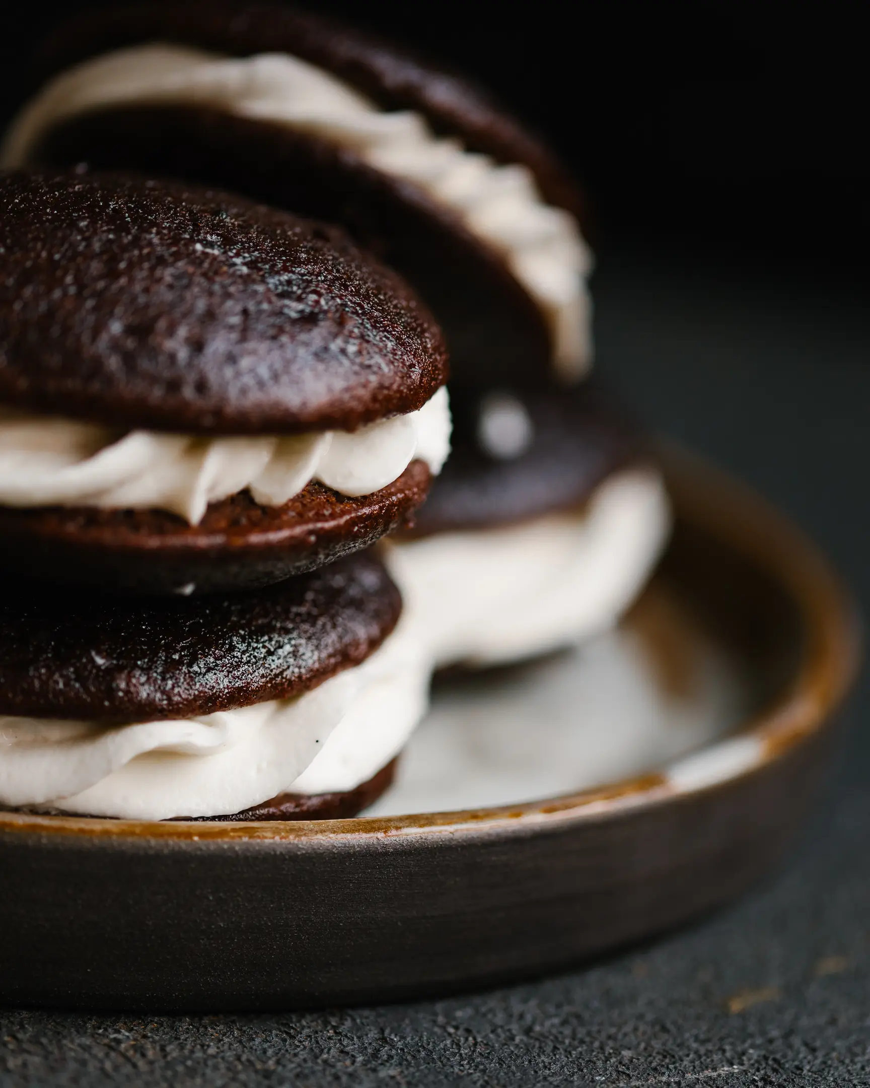 Шоколадови пайове лежат върху керамична чиния.  Whoopie-pies лежат в керамична чиния. Редят се с маслен крем.