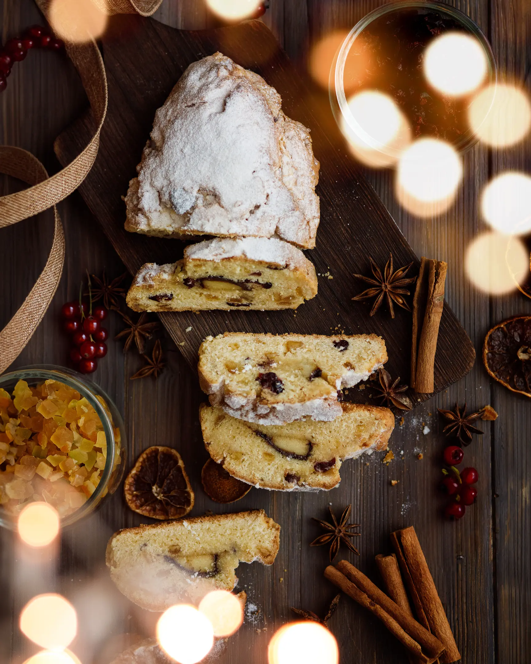 Cut curd Stollen stands on a wooden table.  View from above Cut curd Stollen stands on a wooden table. Around it lie cinnamon and other spices, as well as candied fruits and ribbons for packaging.