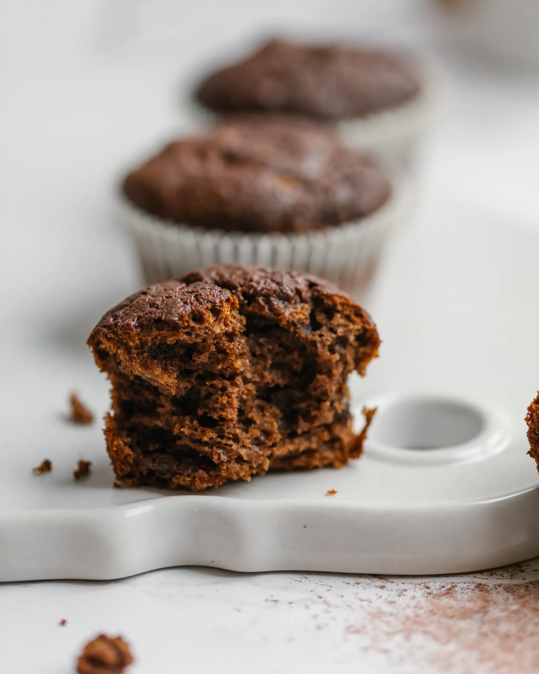 Texture of muffins On a light table on a white ceramic cutting board there are chocolate-colored cupcakes. They was cut. They are made without flour, eggs or refined sugar.