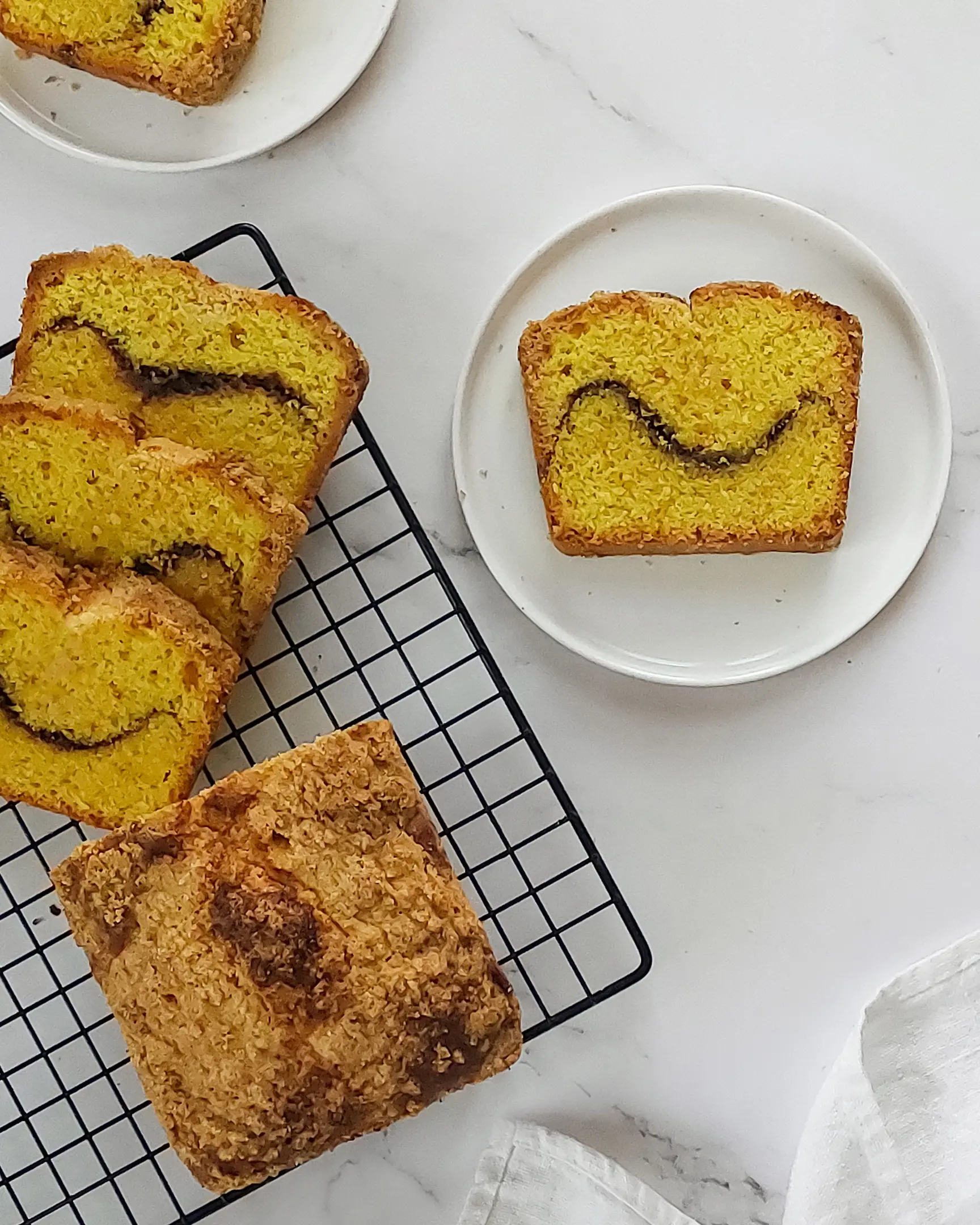 There is a cut cupcake with cinnamon waves.  On a pastry rack for cooling there is a cut cupcake with cinnamon waves. Next to her is a piece of cupcake on a white plate.