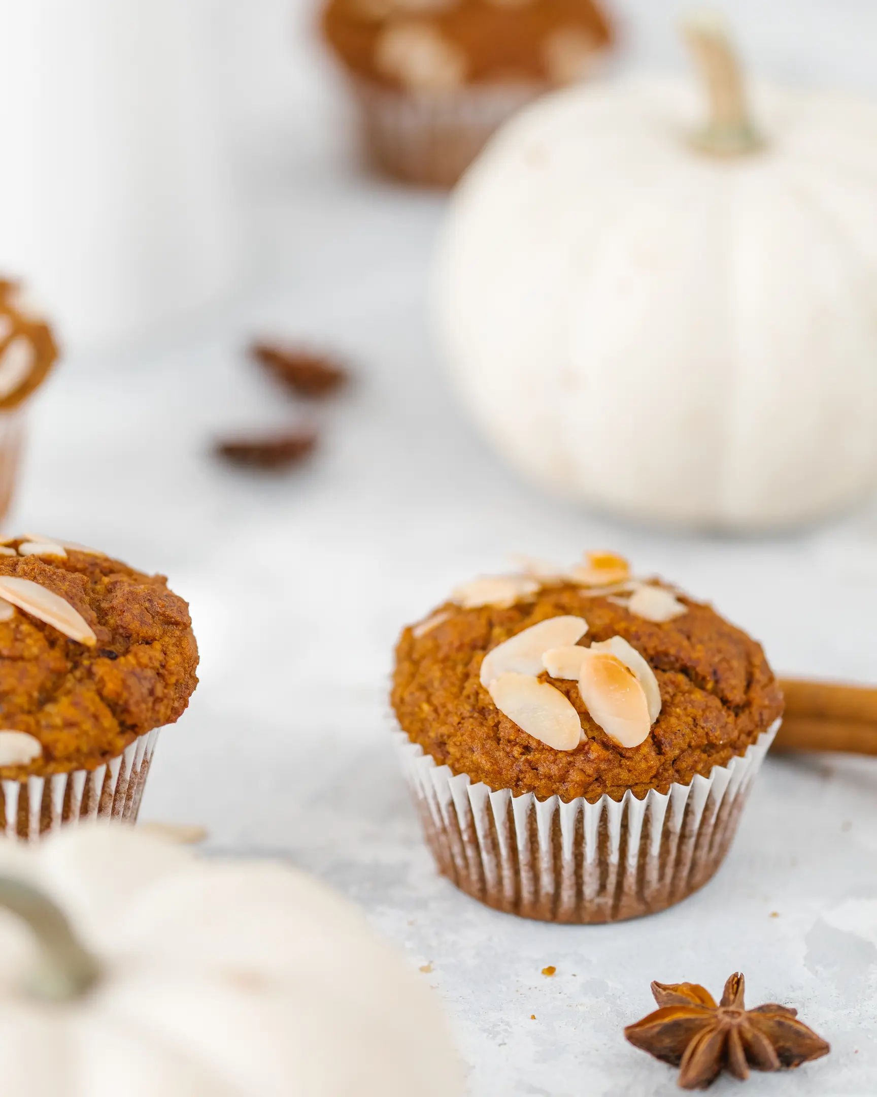 sunny pumpkin muffin On a light table there is a sunny pumpkin muffin, it is decorated with slivered almonds. There are white pumpkins and a milk jug in the background.