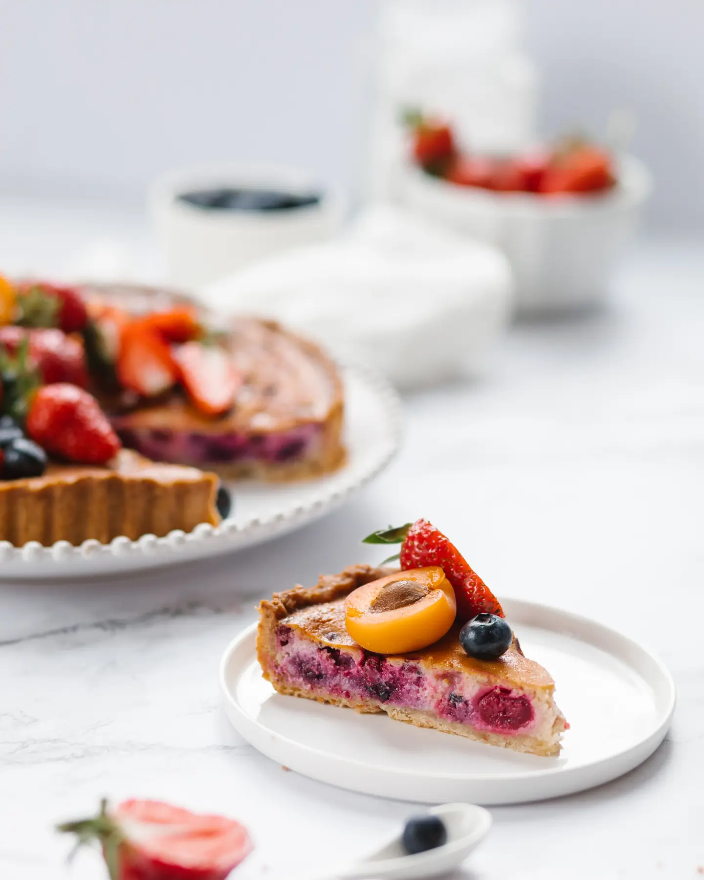 The pie with berries and frangipane cut. A round pie with berries is on the table. It has a golden brown crust. The pie is decorated with berries. The pie is cut.